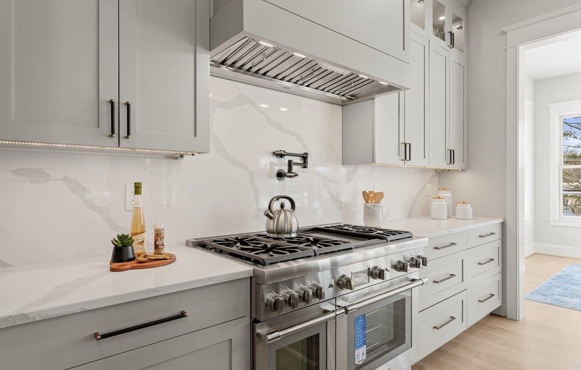 Modern kitchen with gray cabinets, white countertops, stainless steel stove, and marble backsplash.