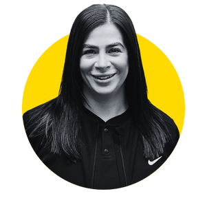 Smiling woman in black with long dark hair, against a yellow circle, wearing a Nike jacket.