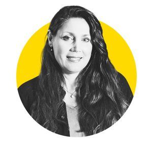 Woman with long, wavy dark hair smiling, wearing a dark jacket, set against a yellow circle.