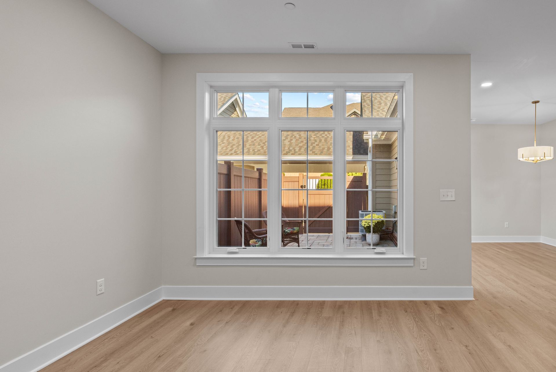 Empty living room with a large front window, light wood floors, and white walls