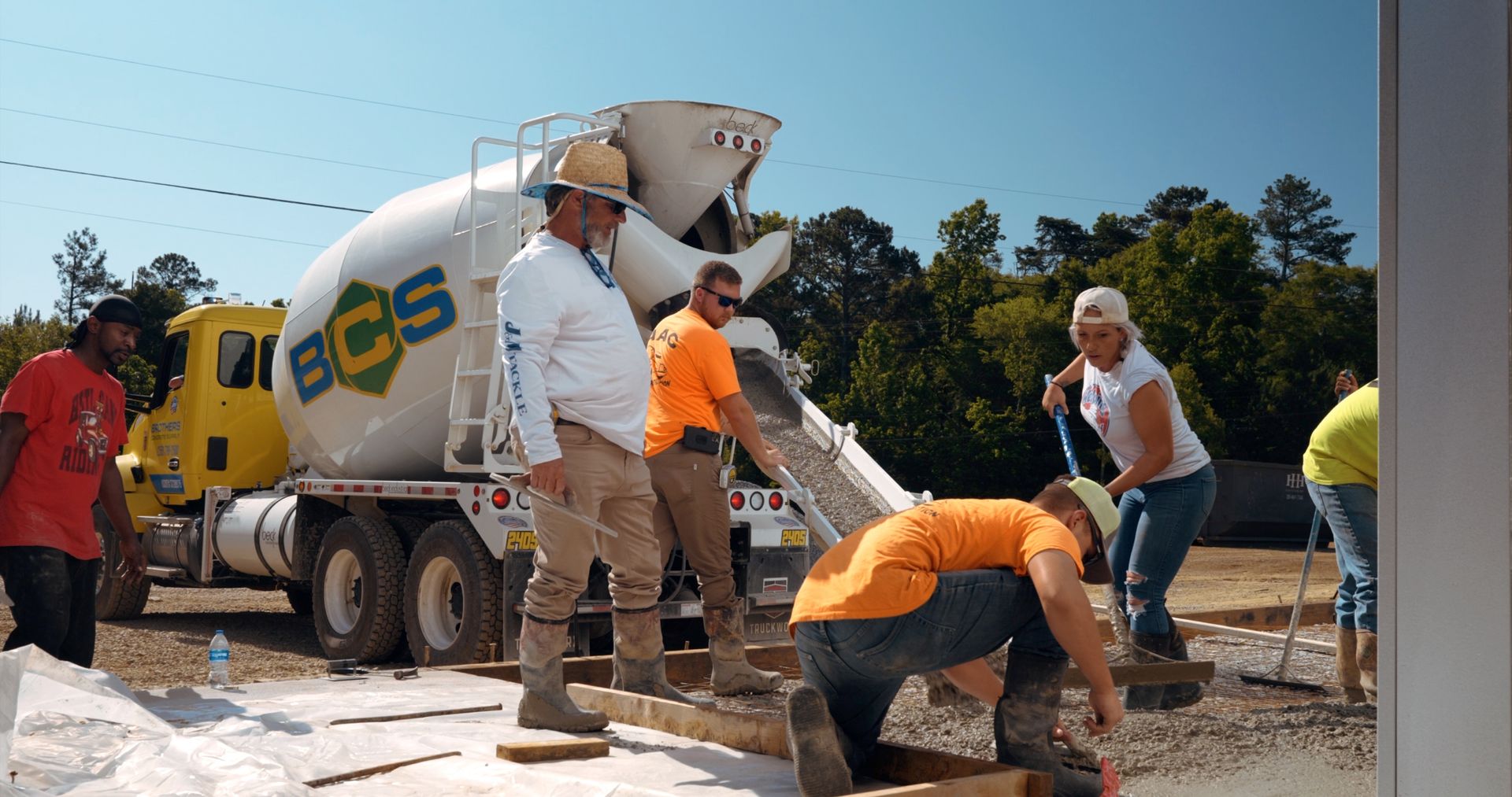 A group of construction workers are working in front of a bcs cement truck