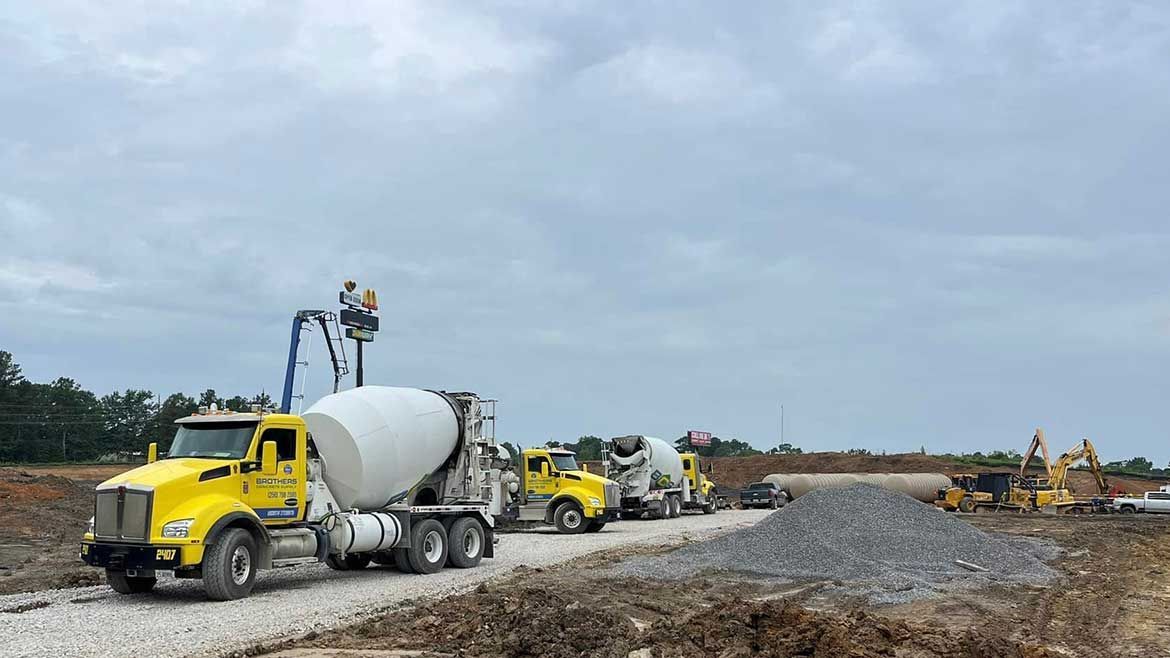 A row of concrete trucks are driving down a dirt road.