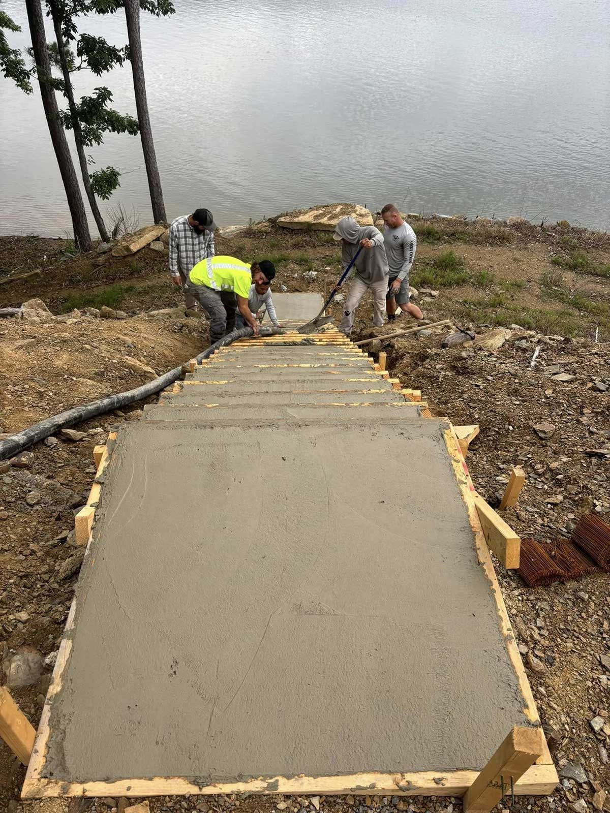 A group of men are working on a concrete walkway next to a body of water.
