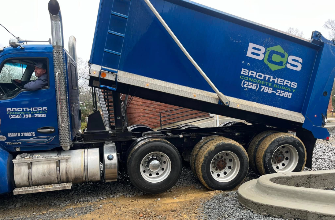 A blue dump truck is driving down a dirt road.