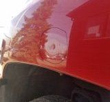 A close up of a red car with a hole in the fender.