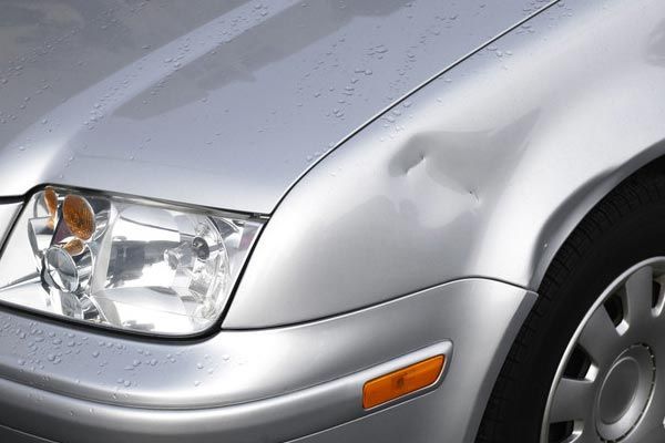 A silver car with a damaged fender and headlight