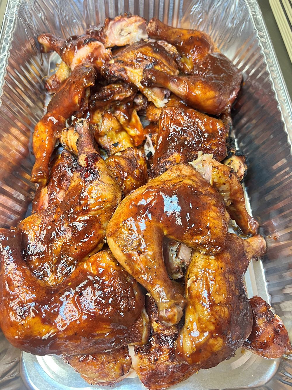 Aluminum foil container filled with chicken covered in barbecue sauce.