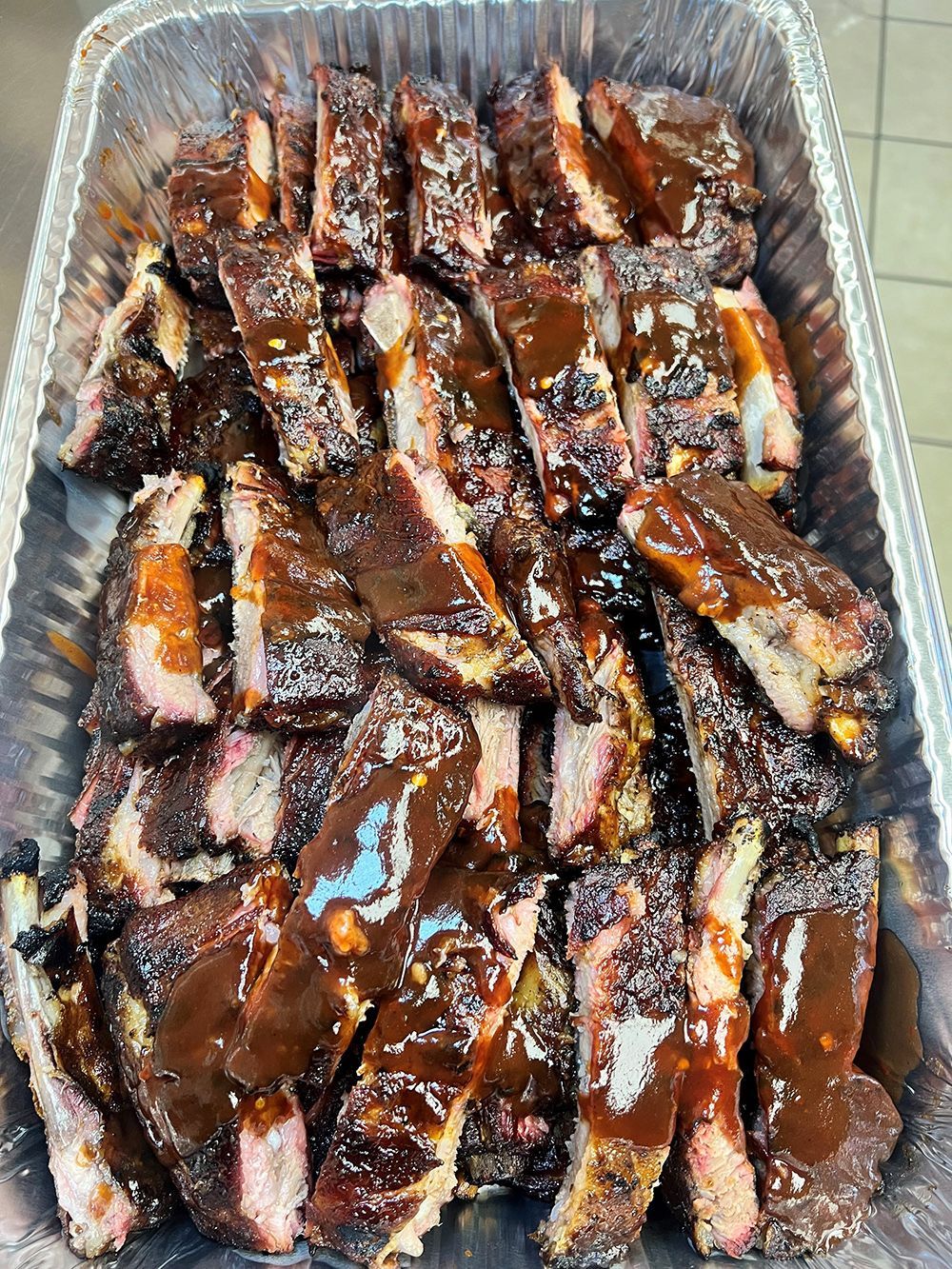 Aluminum foil tray filled with ribs and barbecue sauce.