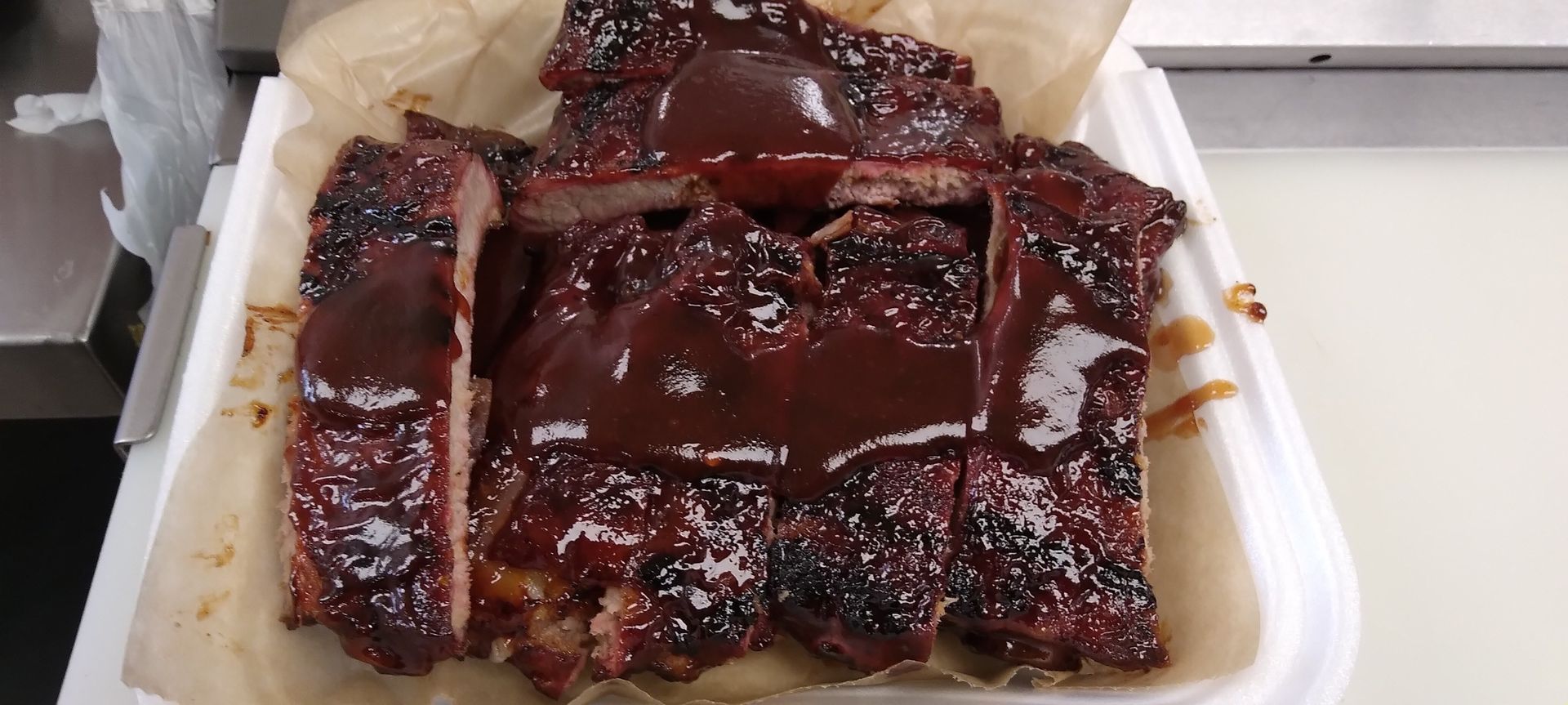 a white styrofoam container filled with ribs and barbecue sauce