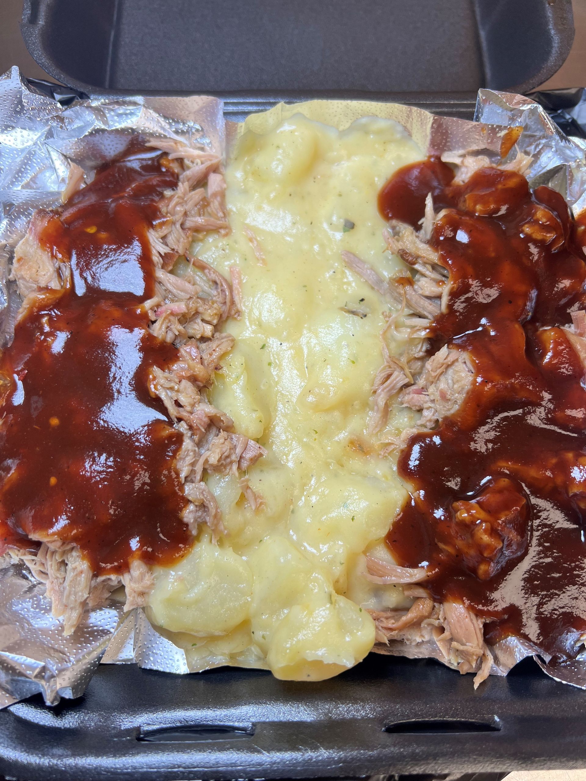 A black styrofoam container filled with meat and sauce.