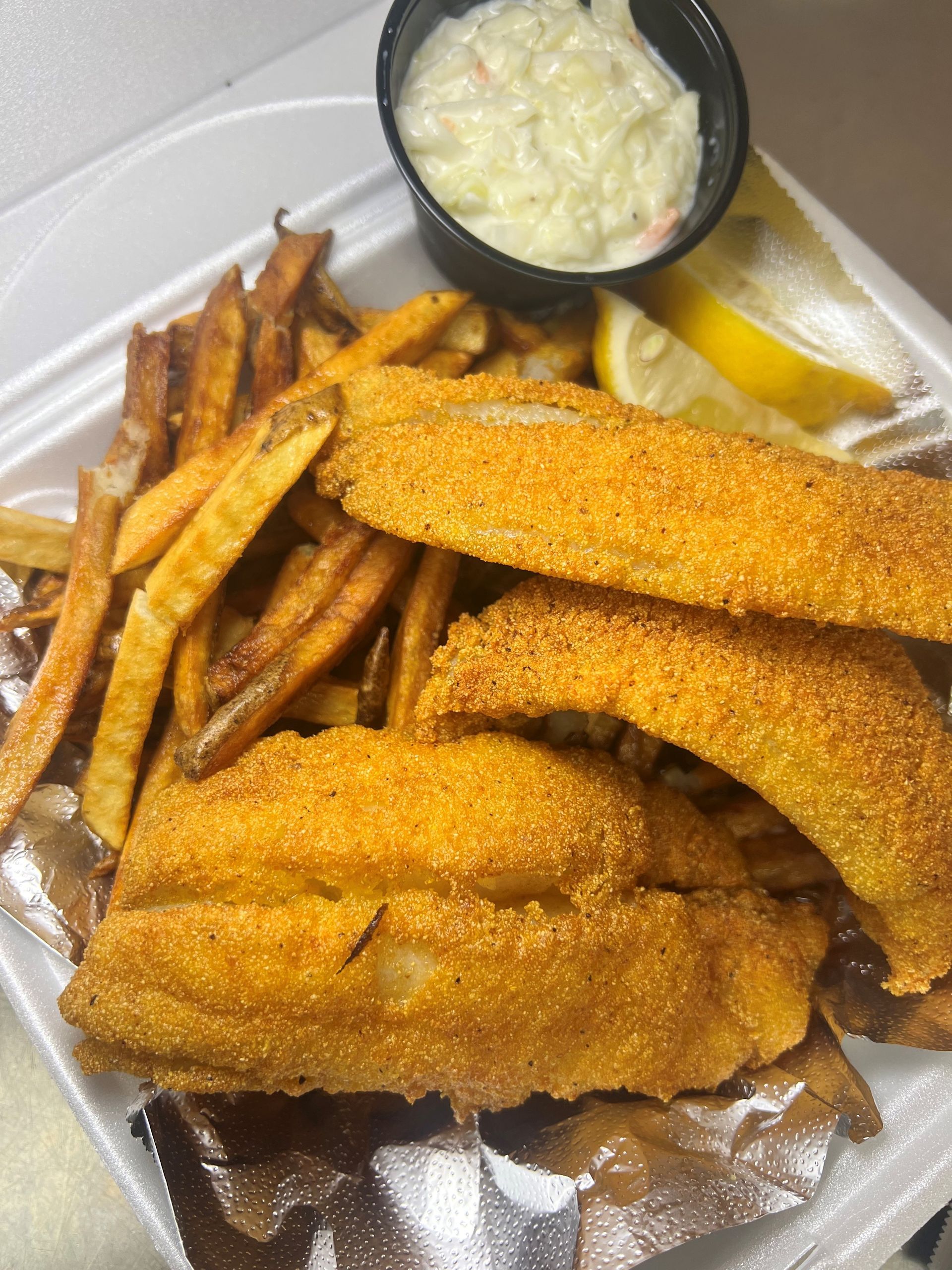 A styrofoam container filled with fried fish and french fries.