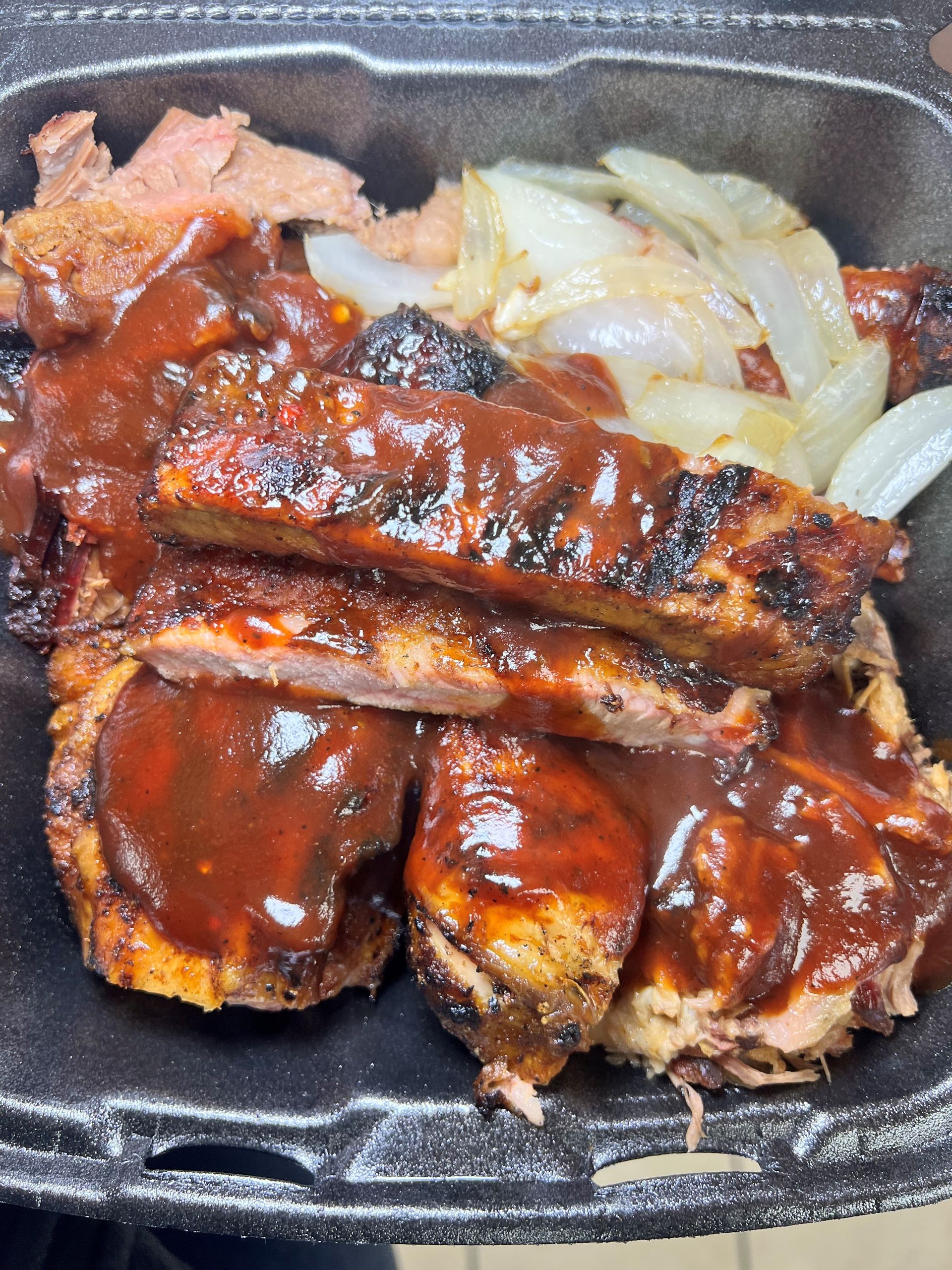 A black styrofoam container filled with meat and sauce.