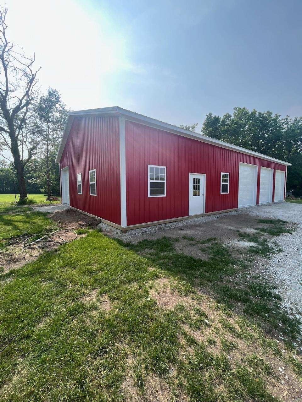 Red metal building with white doors and windows on gravel lot, sunny day.