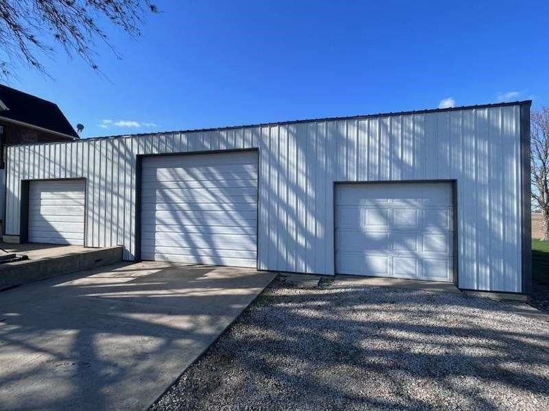 Three-bay white metal garage with gray trim and doors against a blue sky.
