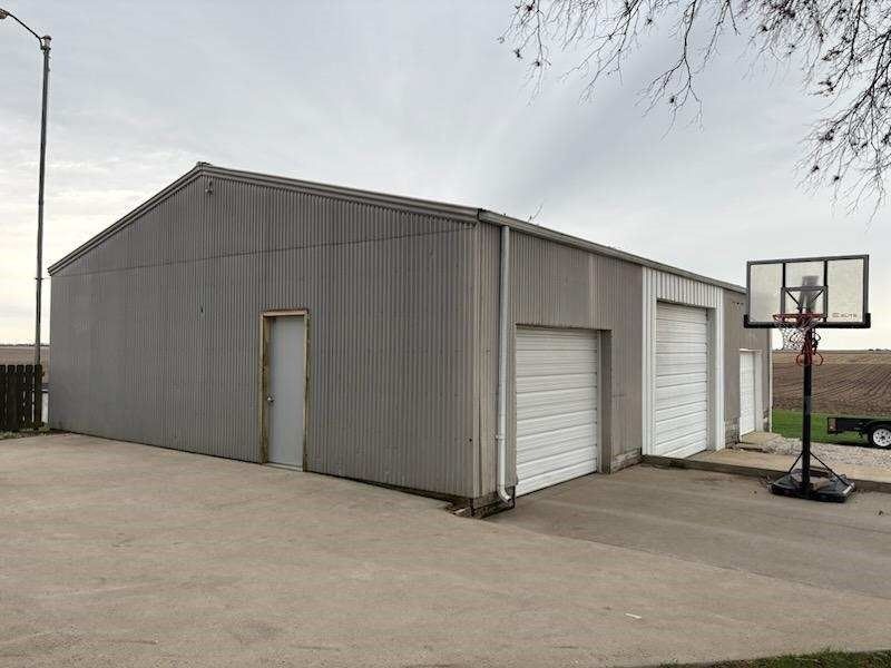 Gray metal building with two garage doors, a side door, and a basketball hoop. Concrete driveway.