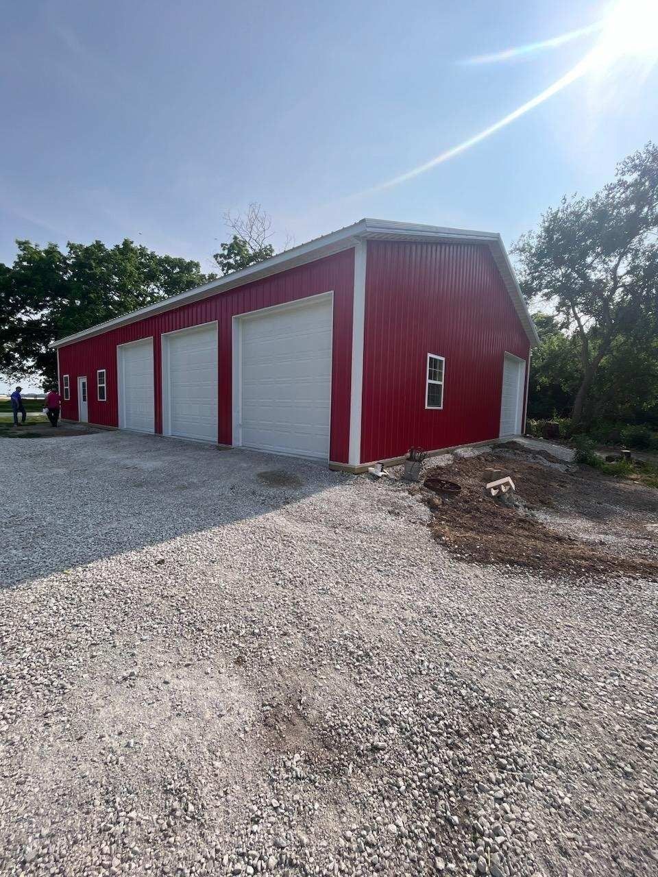 Red metal building with three garage doors and gravel driveway.