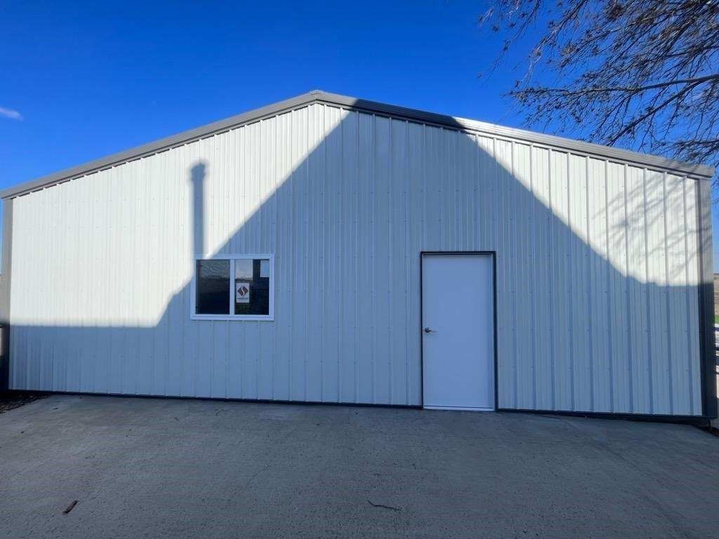 White metal building with a white door and window, under a bright blue sky.