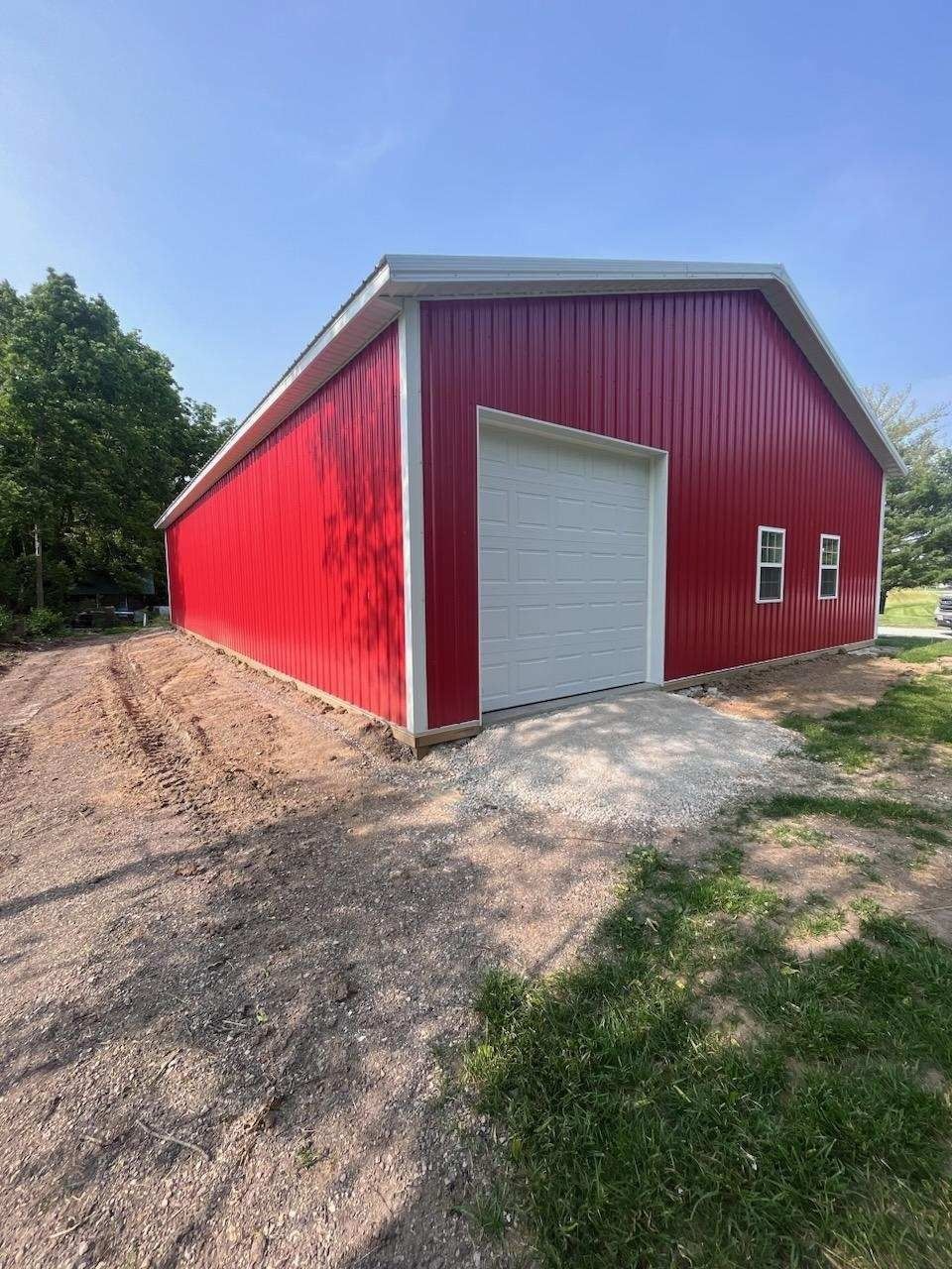 Red metal barn with white trim and garage door, on gravel, under a blue sky.