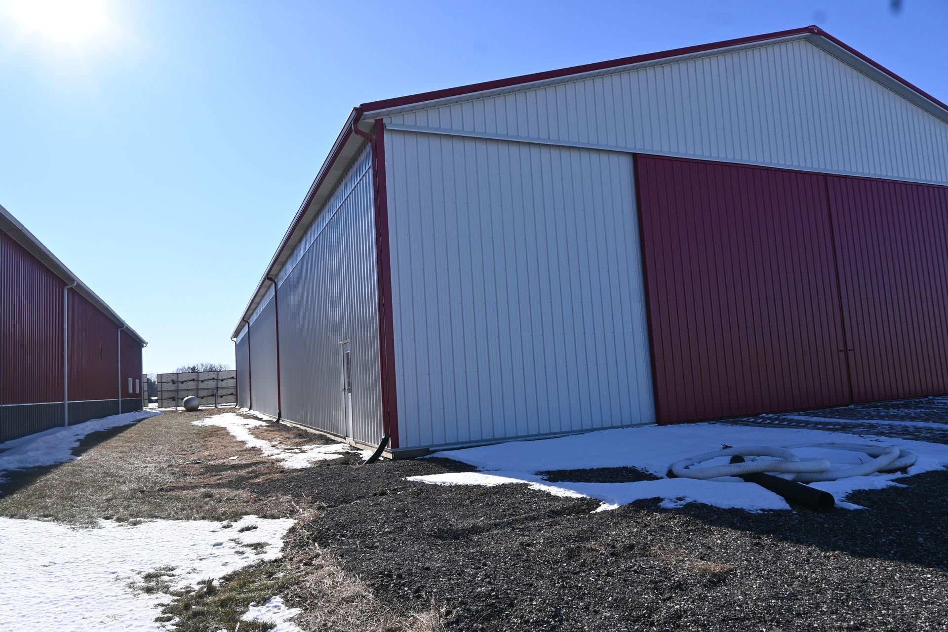 Barns, one red, one white, with snow on the ground on a sunny day.