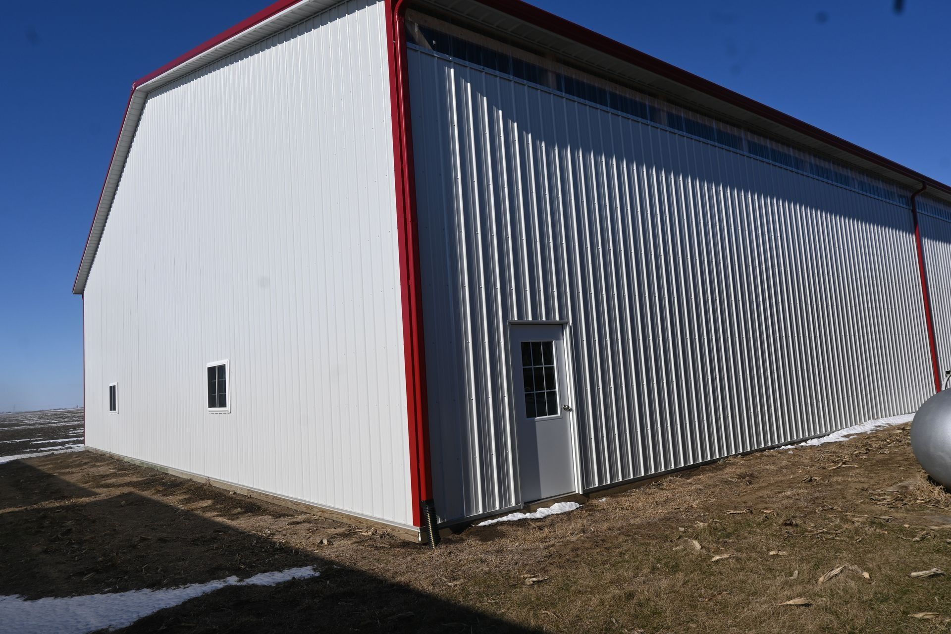 White and red barn building with textured side and small door, clear blue sky.