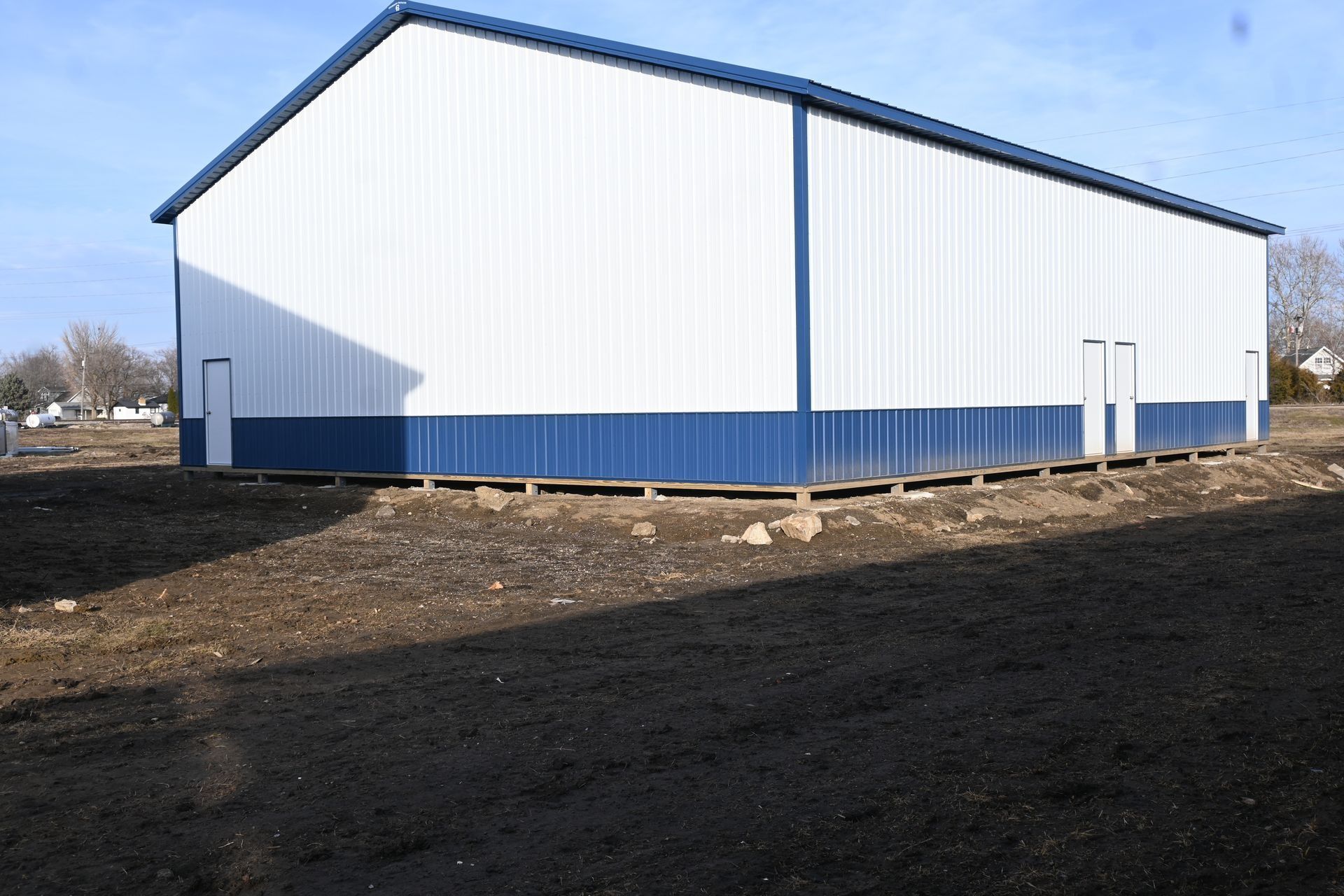 White and blue metal building with a blue roof, standing on a dirt lot under a clear sky.