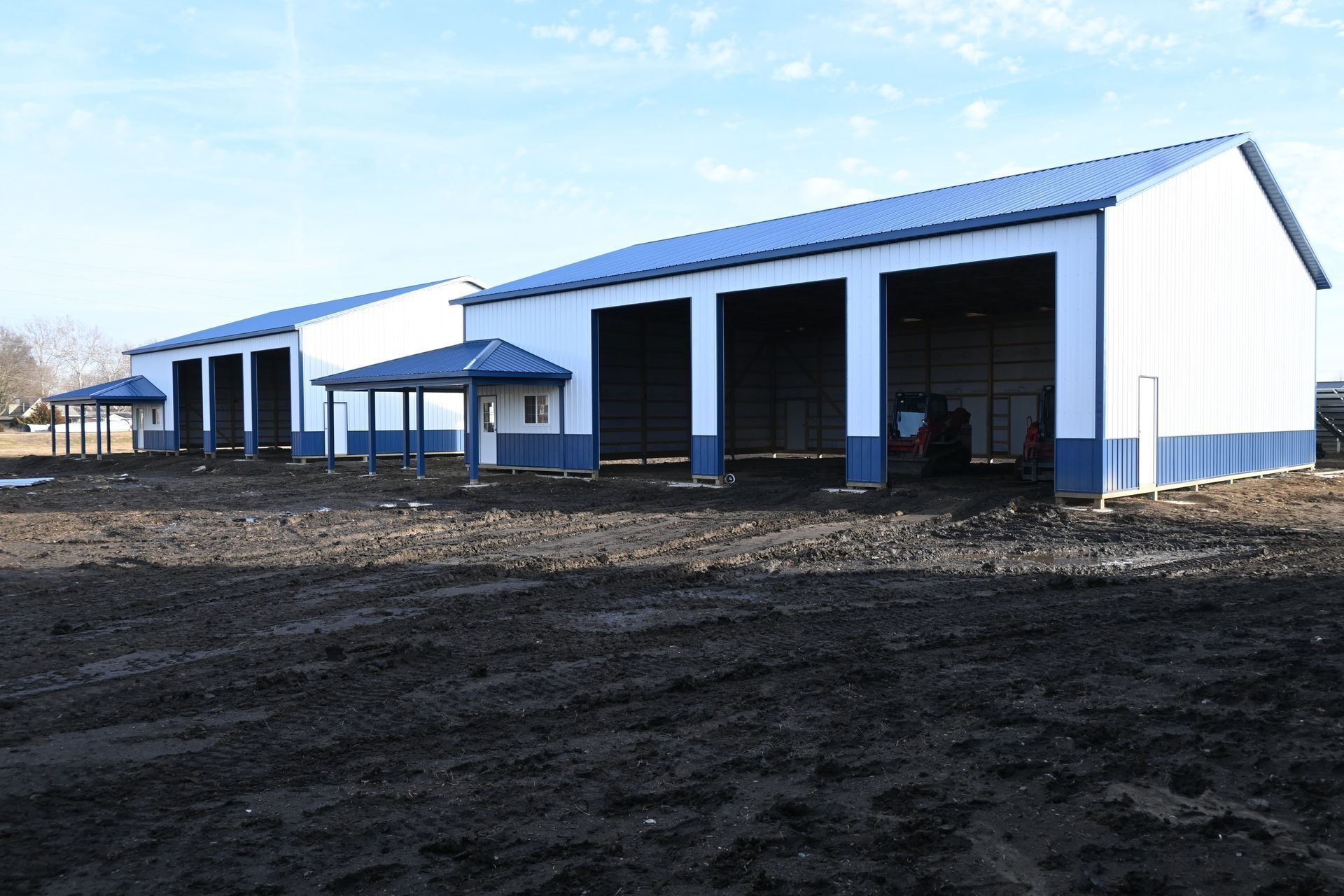 Blue and white metal building with open bays, on a dirt lot.