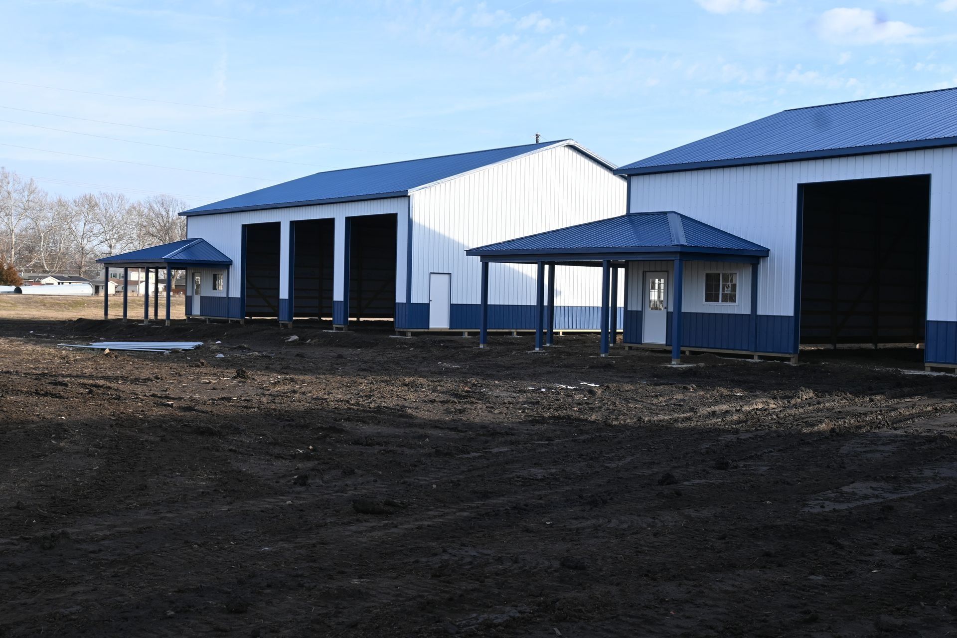 Three white and blue metal buildings with canopies, on a dirt lot, under a blue sky.