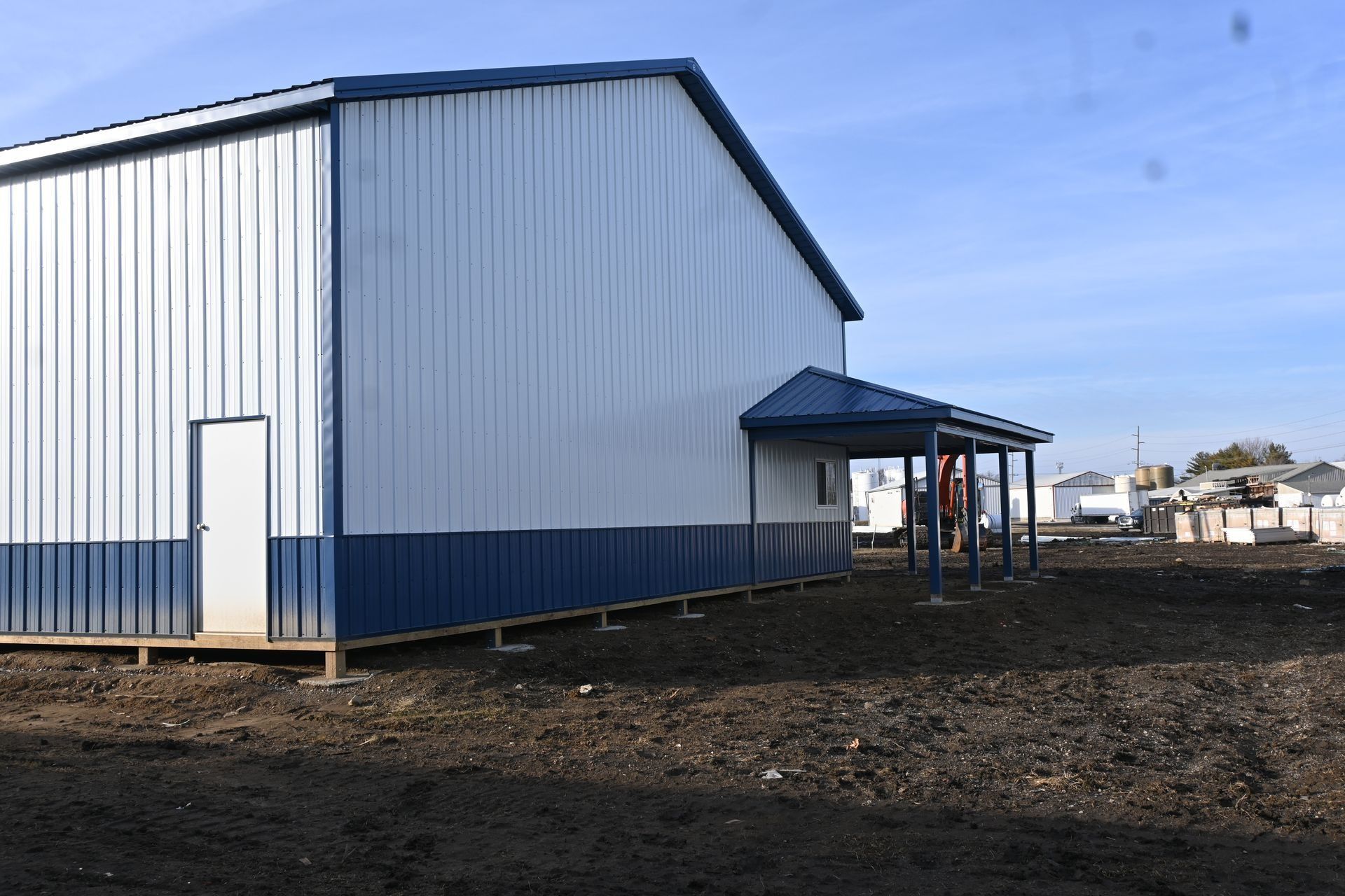 Blue and white metal building with a small awning and a dirt ground.