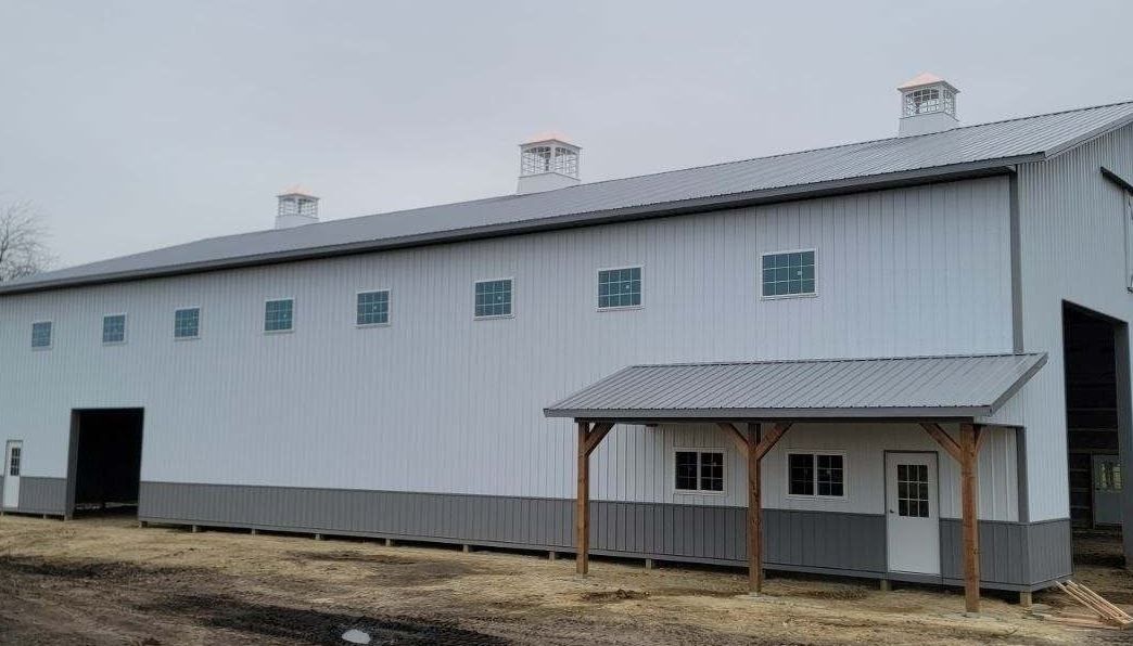 White and gray metal barn with small porch and several windows. Chimneys on roof.