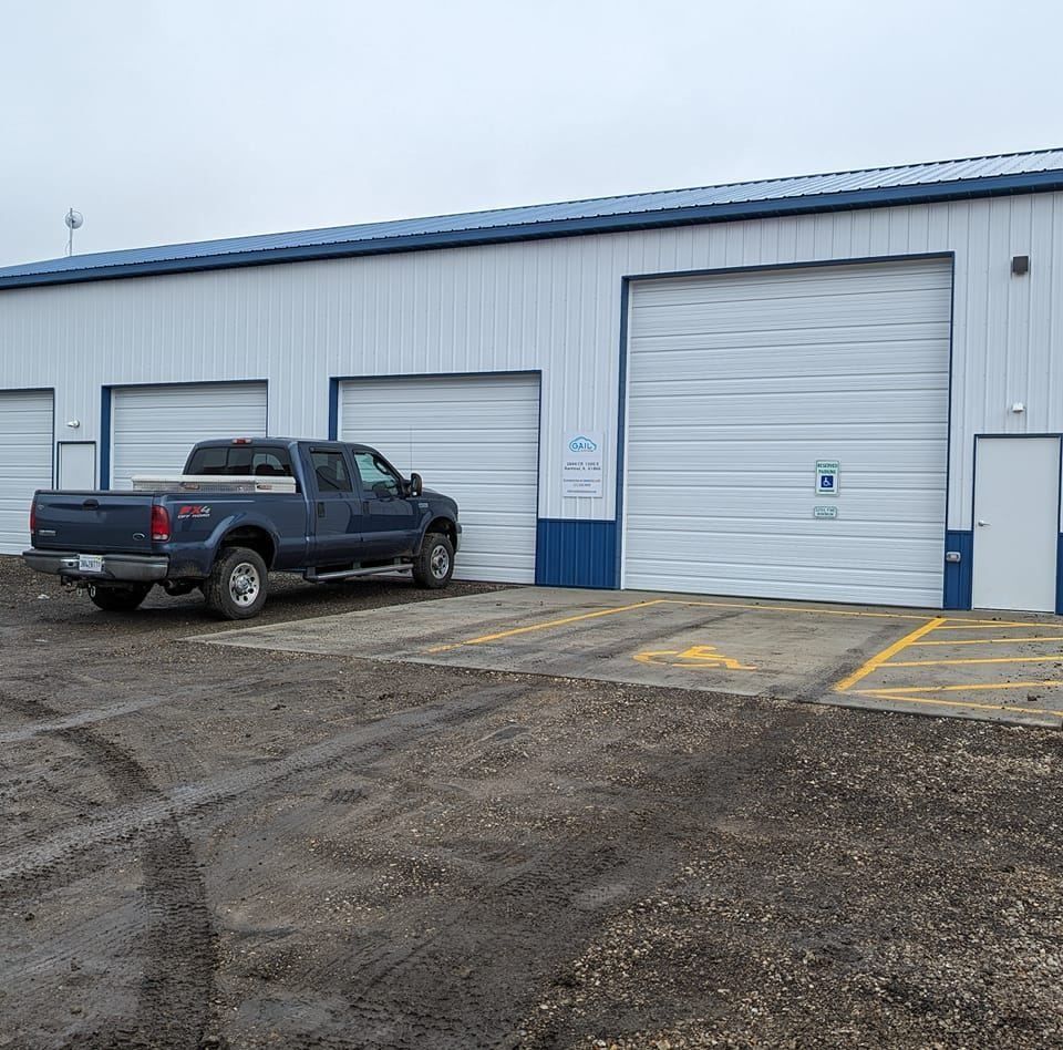 Blue truck parked outside a white industrial building with garage doors; cloudy sky.