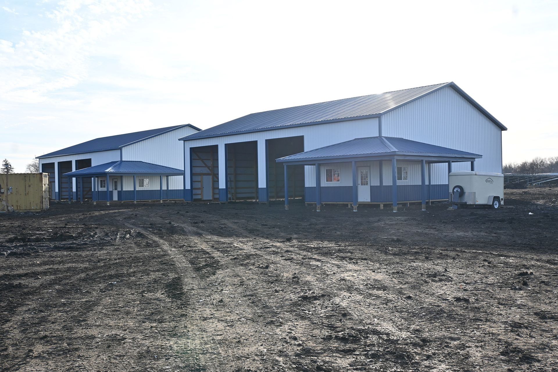 White industrial buildings with blue trim and gazebos on a dark dirt lot under a bright sky.