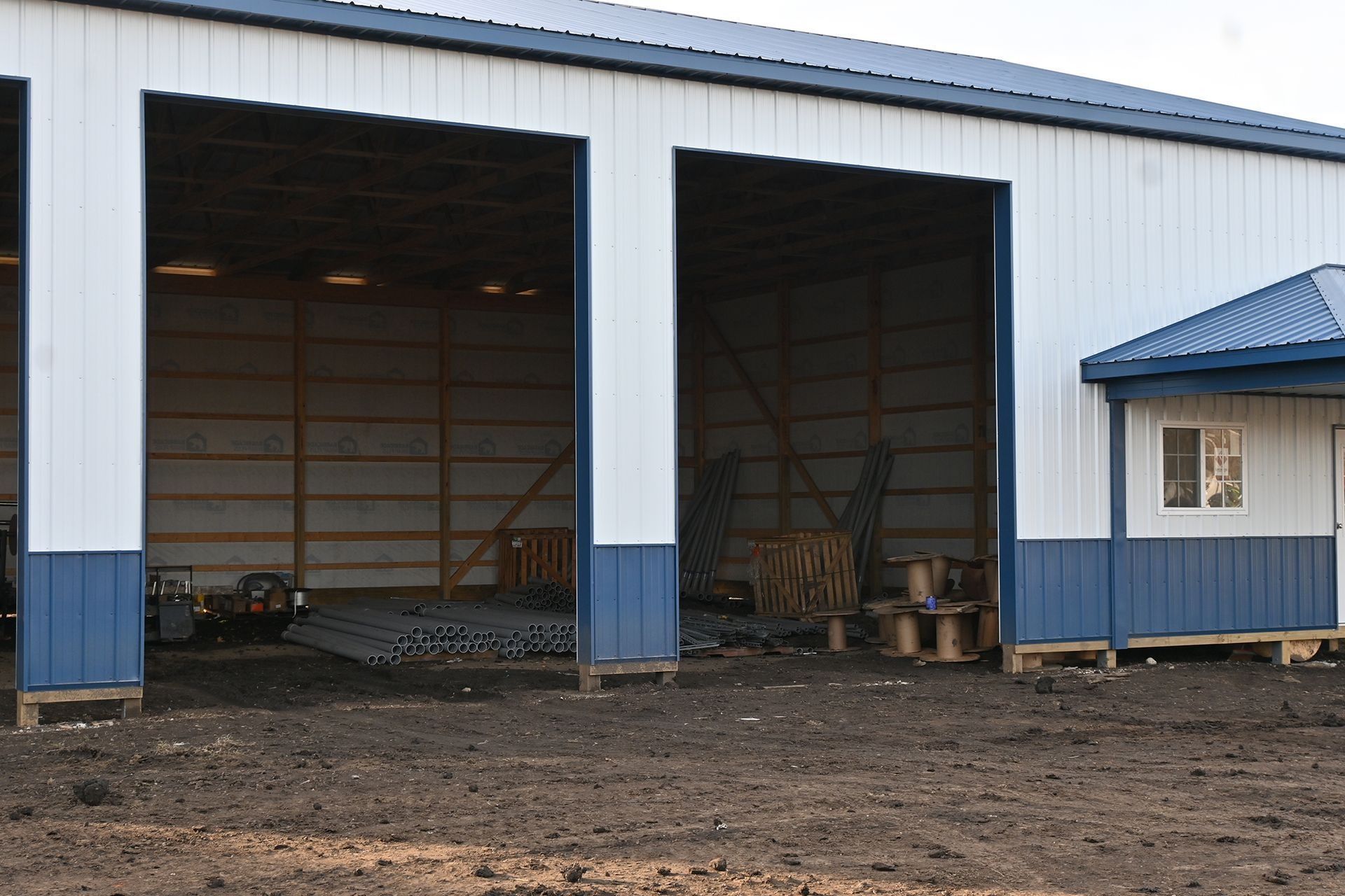 Blue and white metal building with open bays, dirt ground, and a small side structure.
