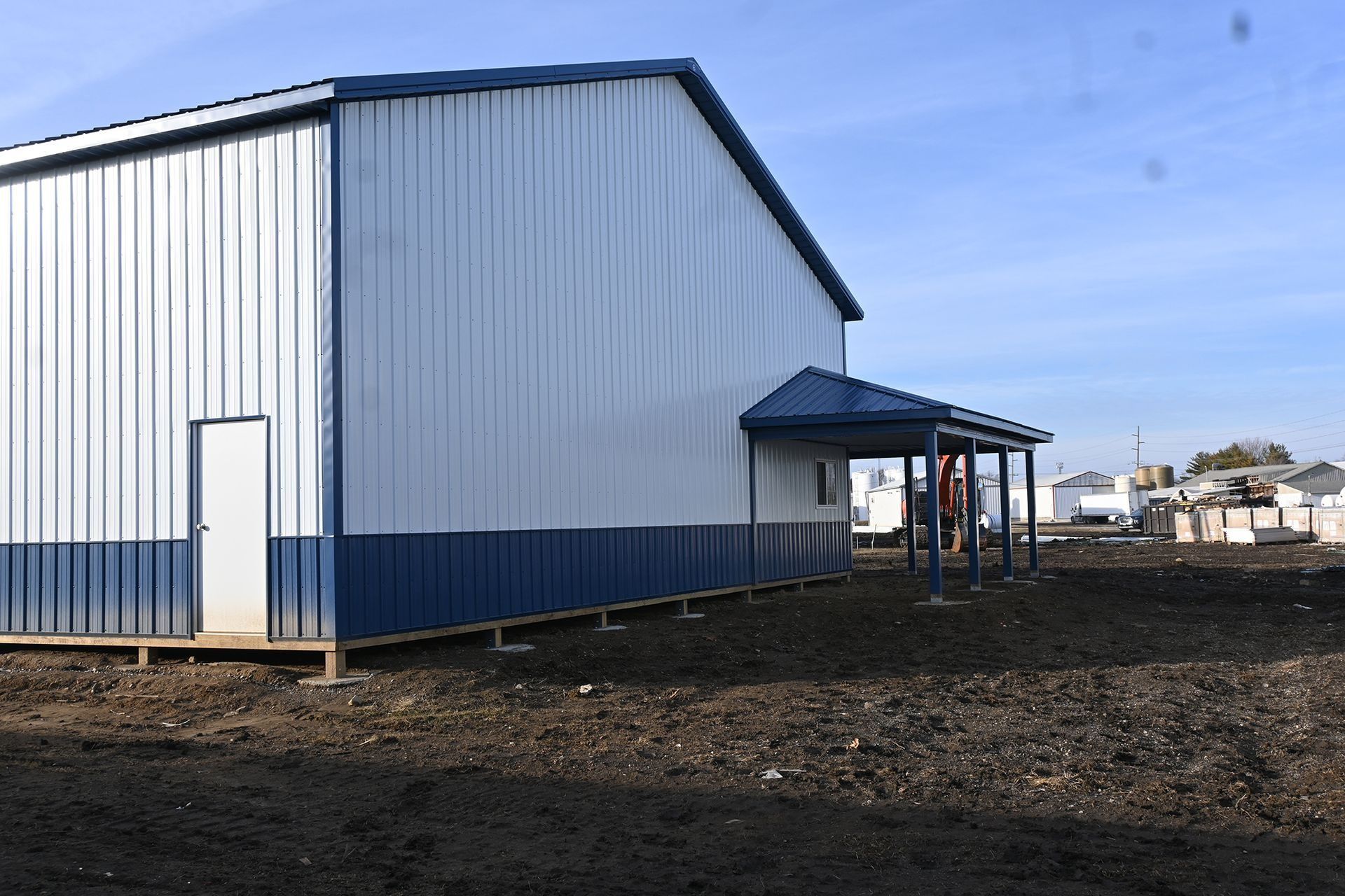 Blue and white metal building with a small awning; set in a dirt lot.