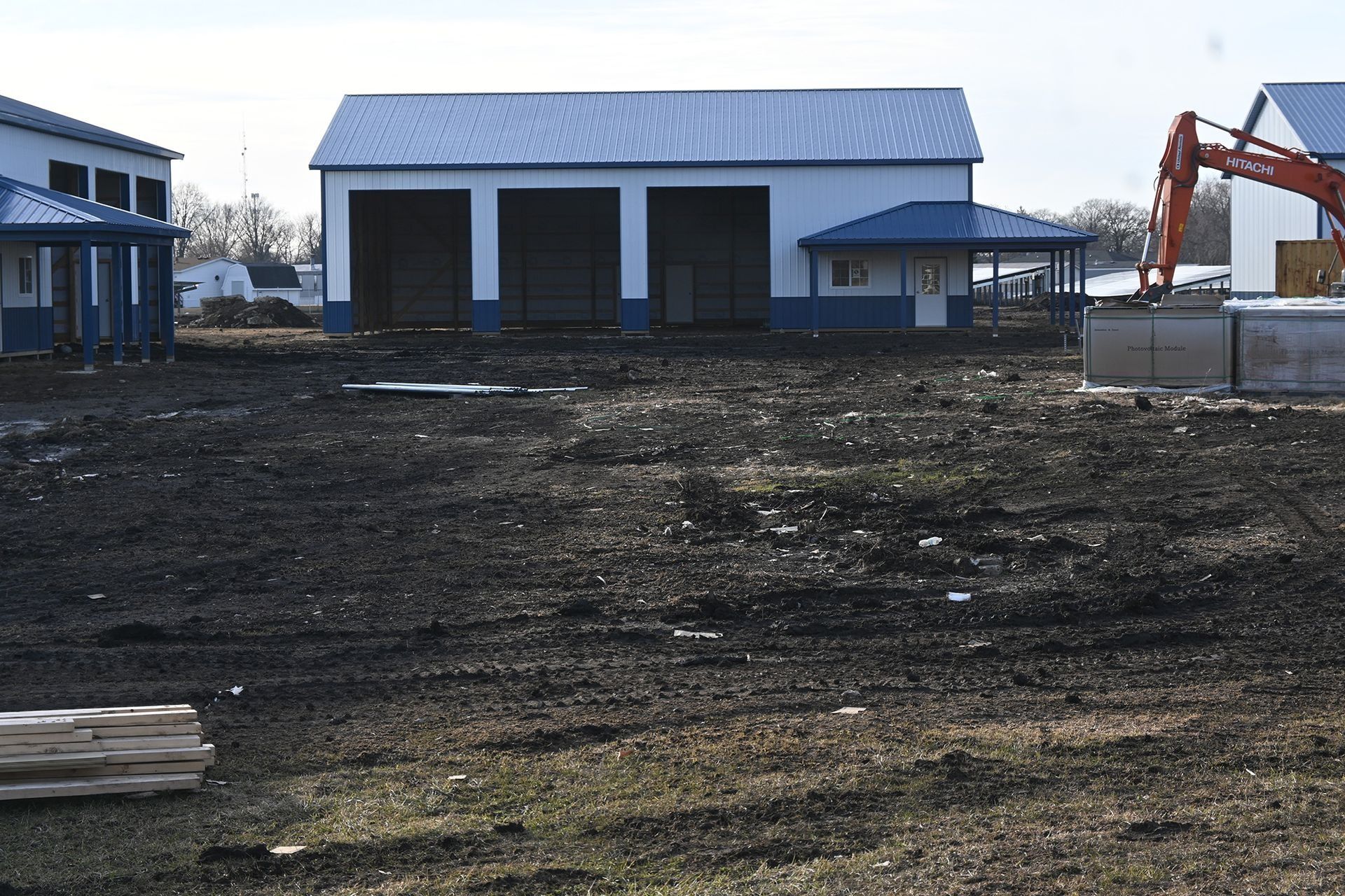 New construction site with blue-trimmed white buildings, including a garage, and an excavator.