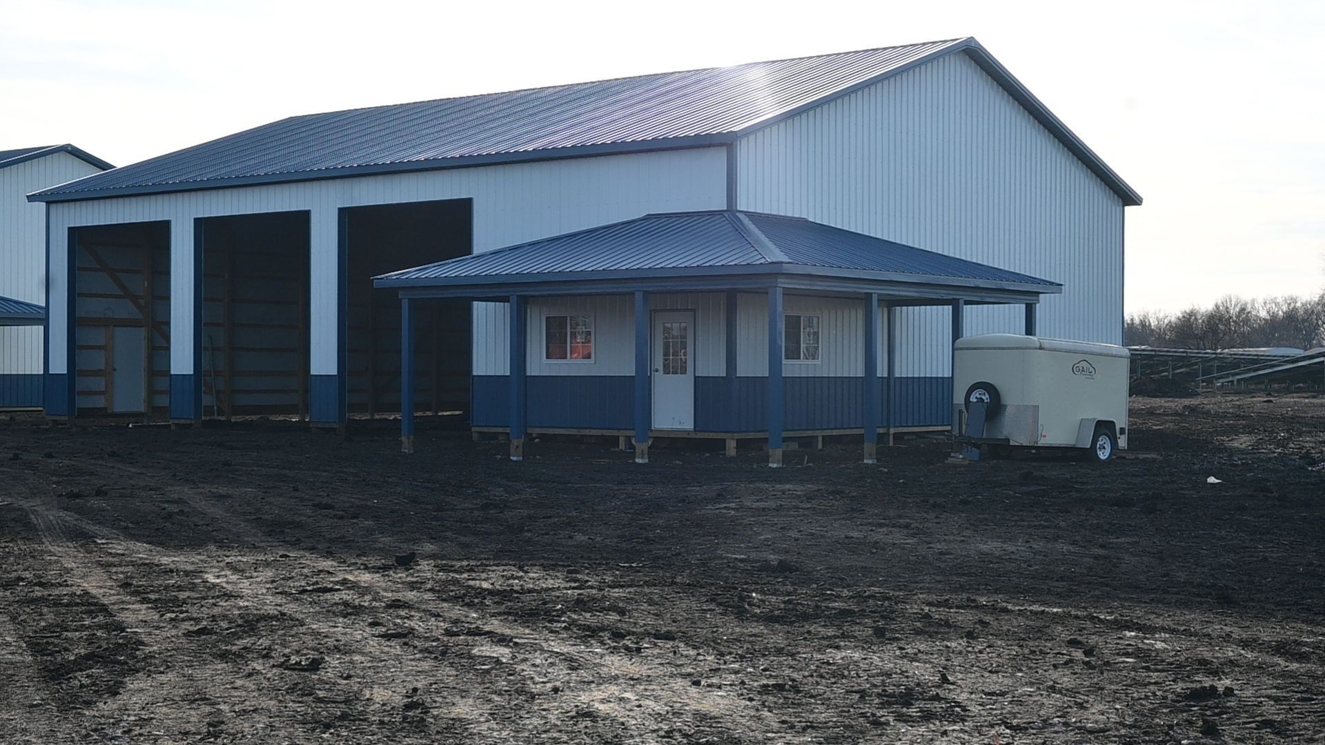 White and blue industrial building with small adjacent structure, set in muddy area.