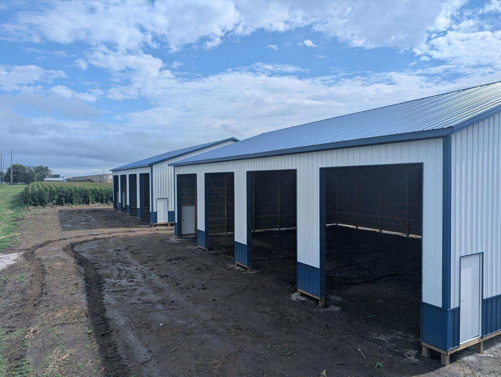 Row of white and blue open-front metal storage sheds with dark gray interiors and blue roofs under a partly cloudy sky.