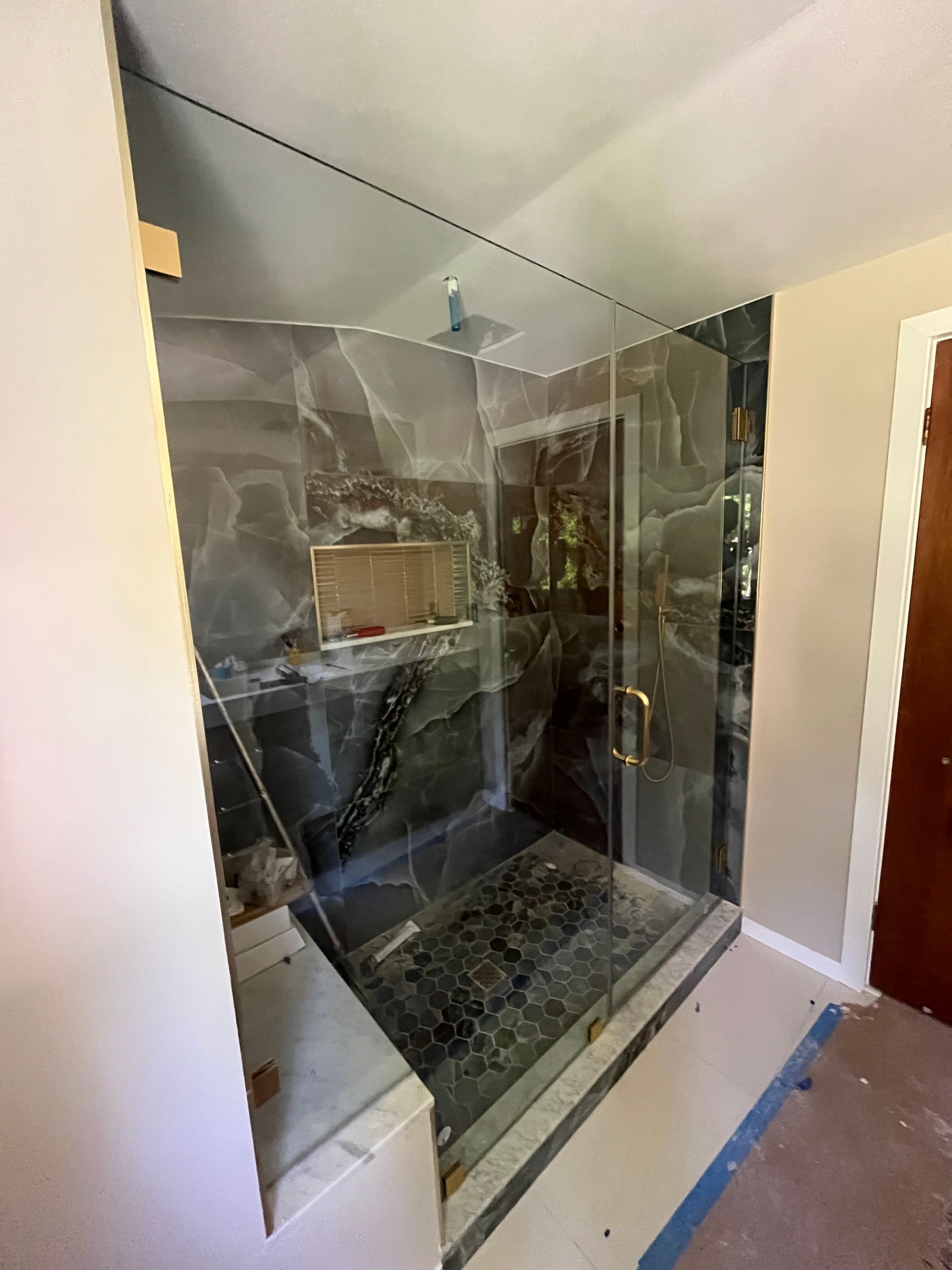 Glass shower enclosure in a bathroom, with tiled floor and walls under construction.