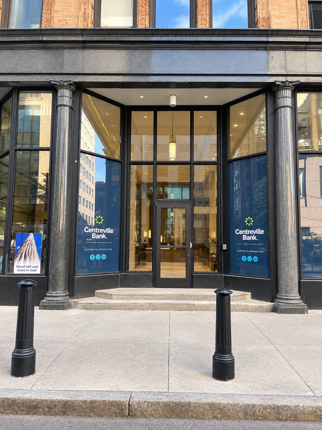 Glass-front entrance to a building with black columns and blue signs beside the doorway