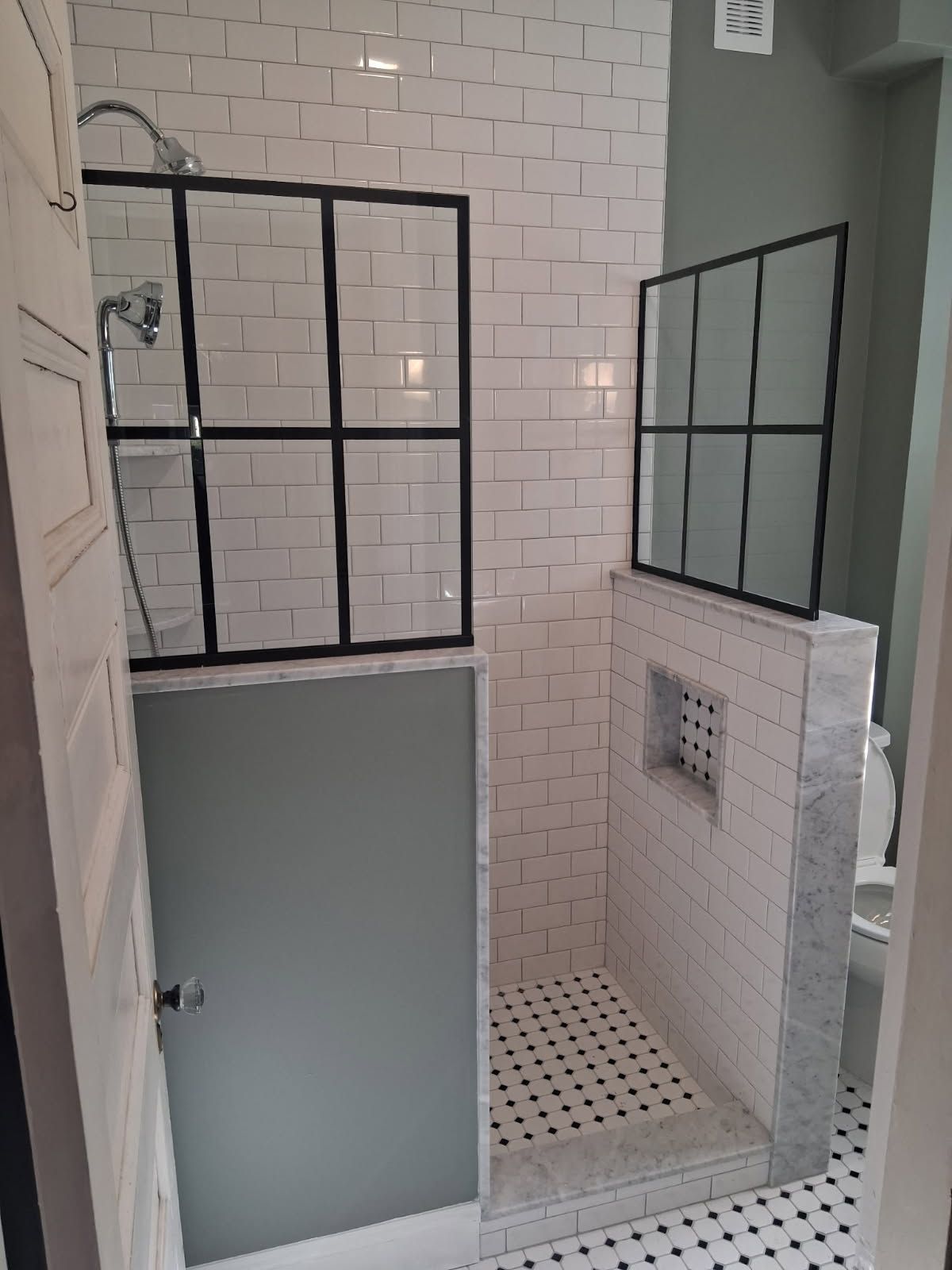 Small tiled shower area with black-framed glass panels and a frosted door.