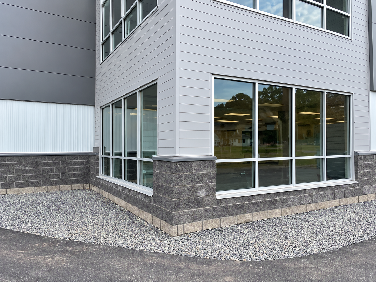 Corner of a modern gray building with large windows and gravel landscaping