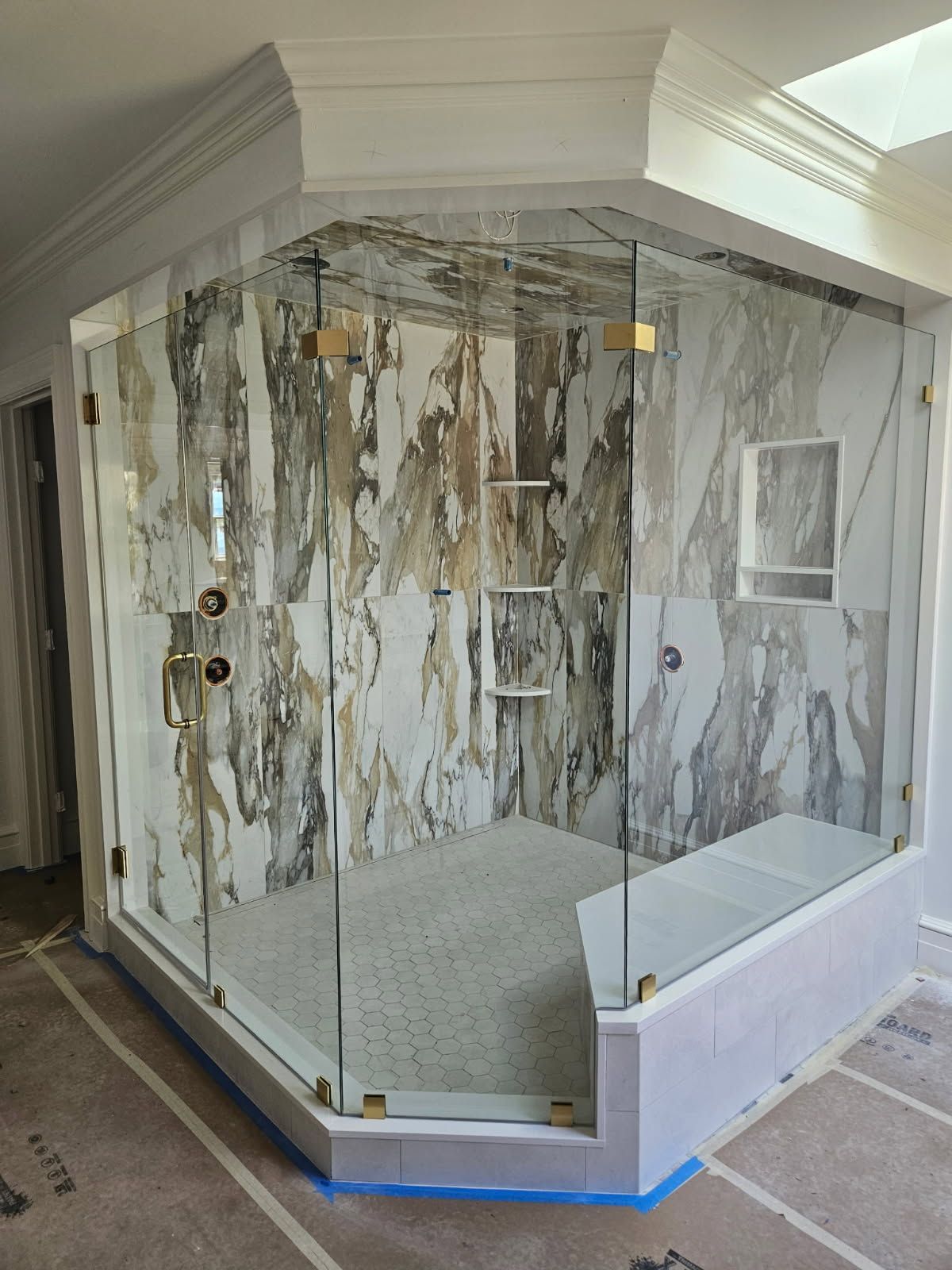 Glass-enclosed marble shower with tiled walls and white base in a bathroom