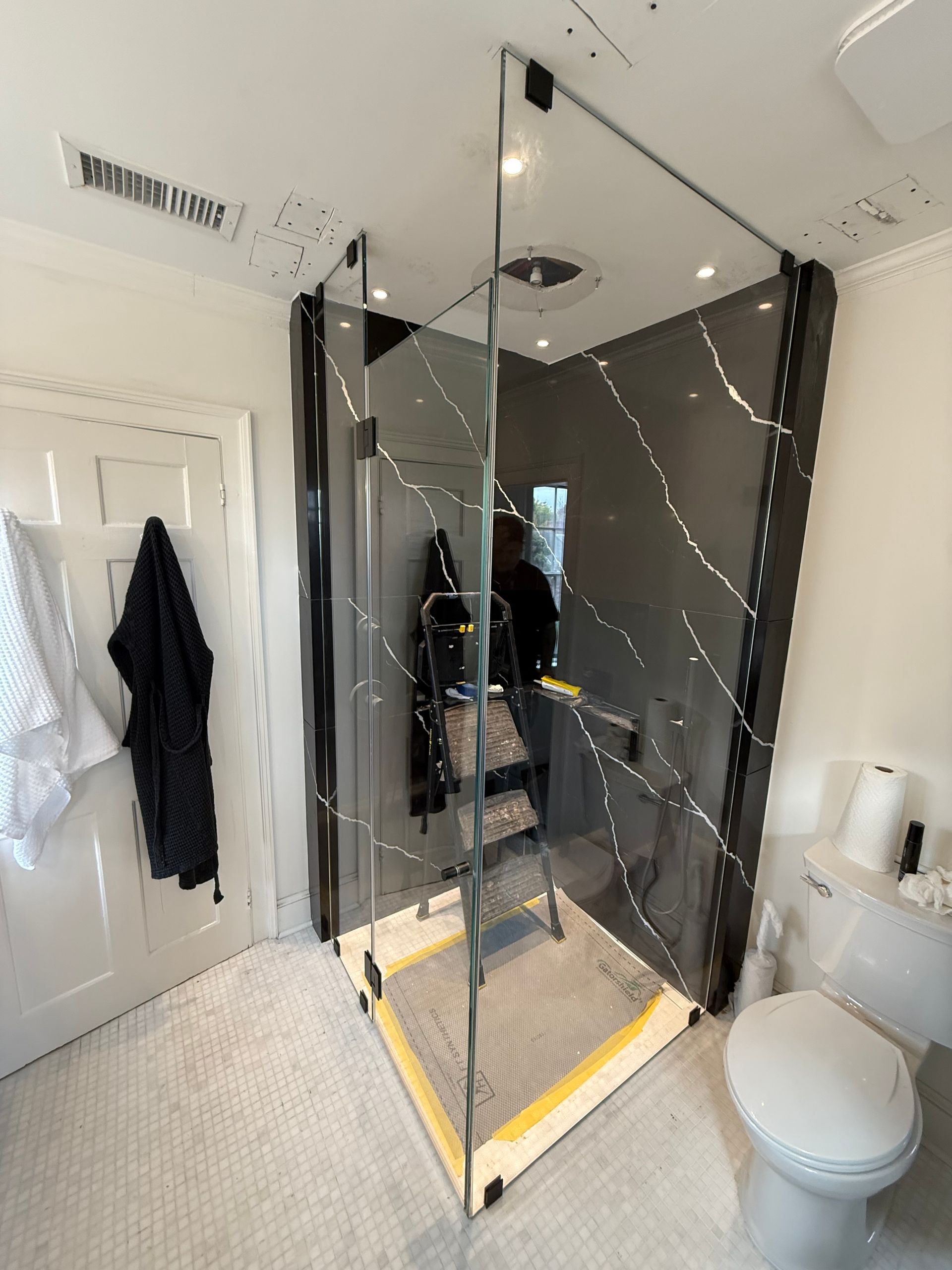 Bathroom with a glass shower enclosure being installed. A person is on a ladder.