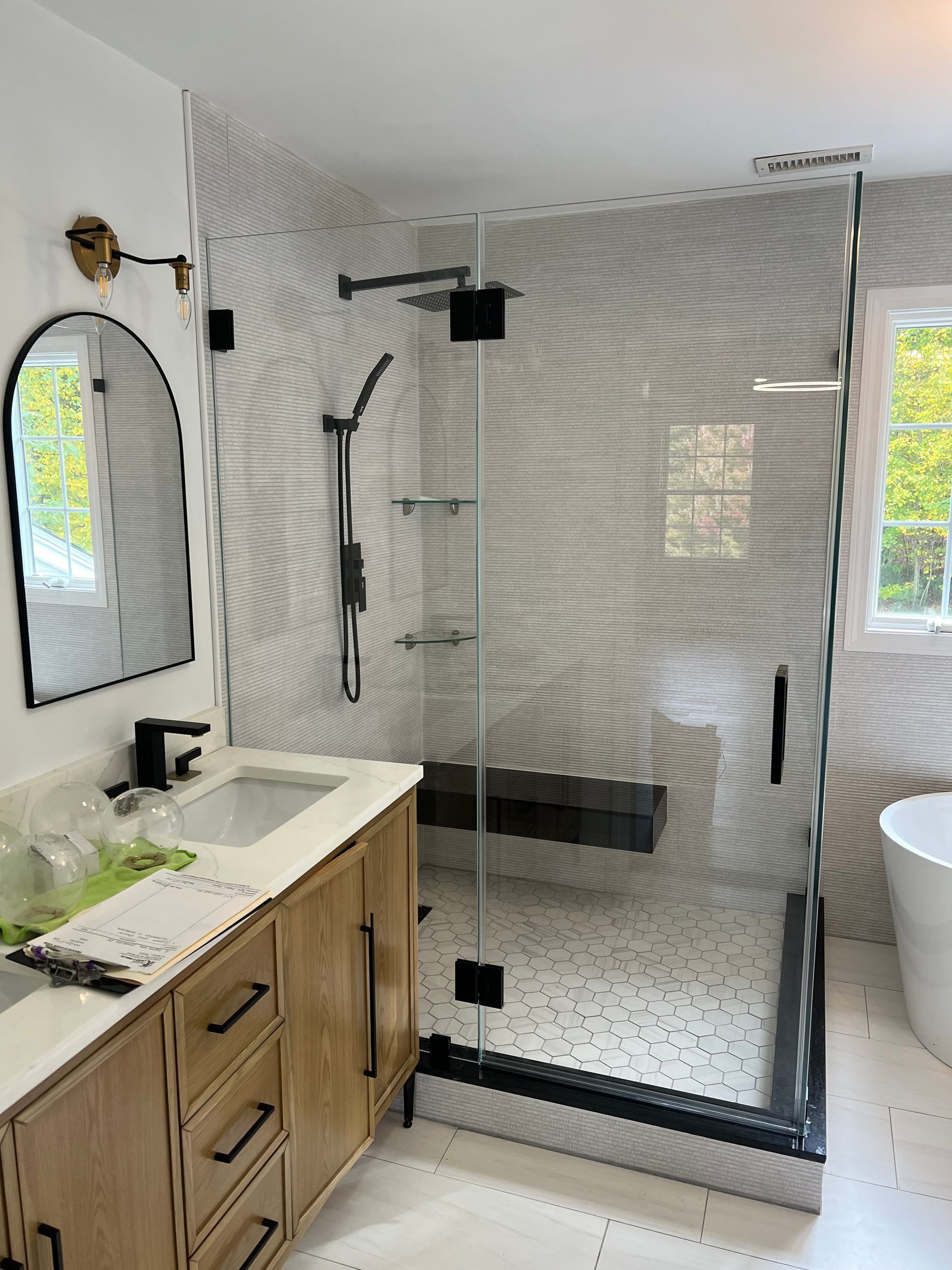 Modern bathroom with glass shower, black fixtures, wooden vanity, and tiled walls.