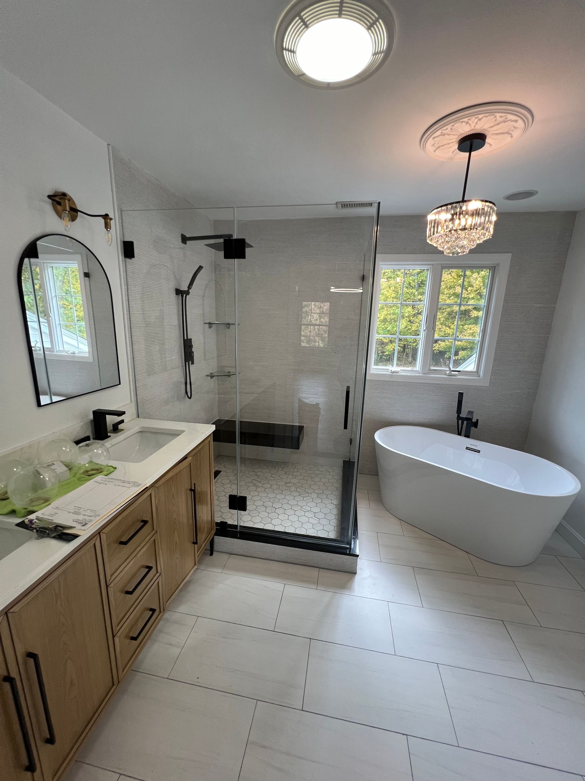 Modern bathroom with a glass shower, soaking tub, and vanity; white tile and light fixtures.