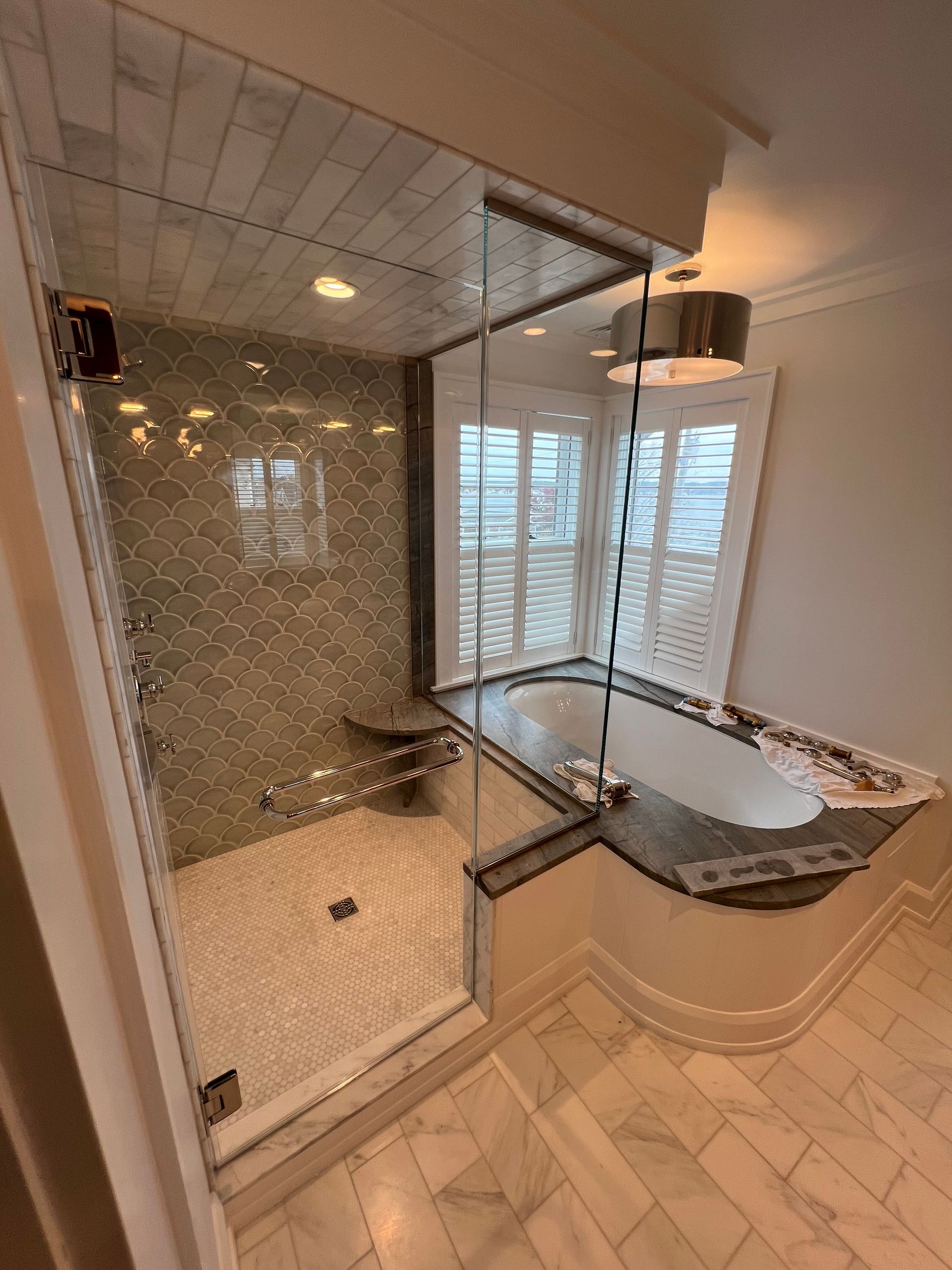 Modern bathroom with a glass shower, a built-in tub, and white marble tile.