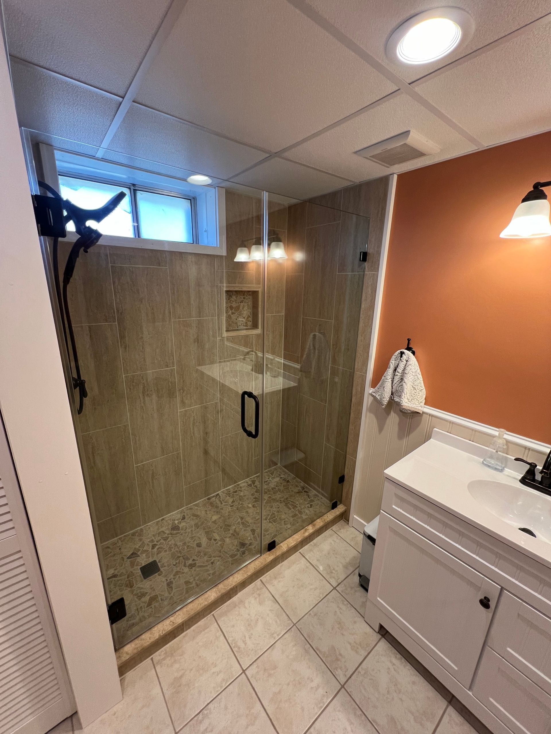 Bathroom with glass shower, neutral tile walls, orange accent wall, and white vanity.