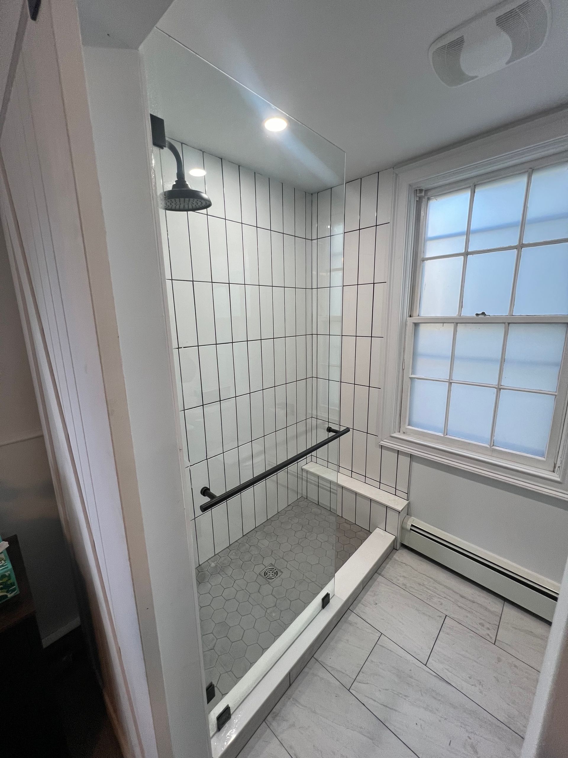 Modern shower with patterned white and black tile, glass enclosure, and window.