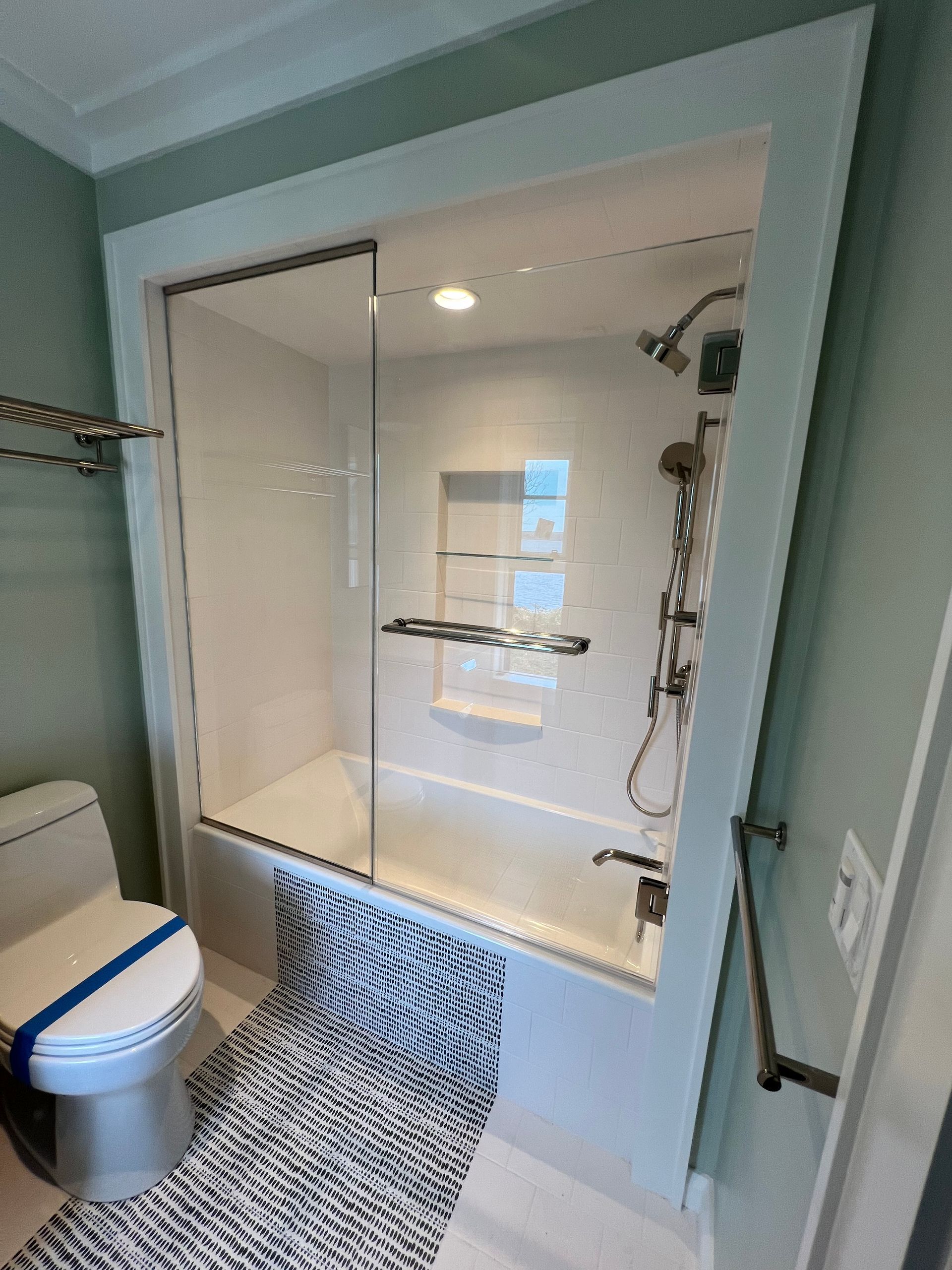 Bathroom with white tub, showerhead, and sliding glass door. A toilet and rug are visible.