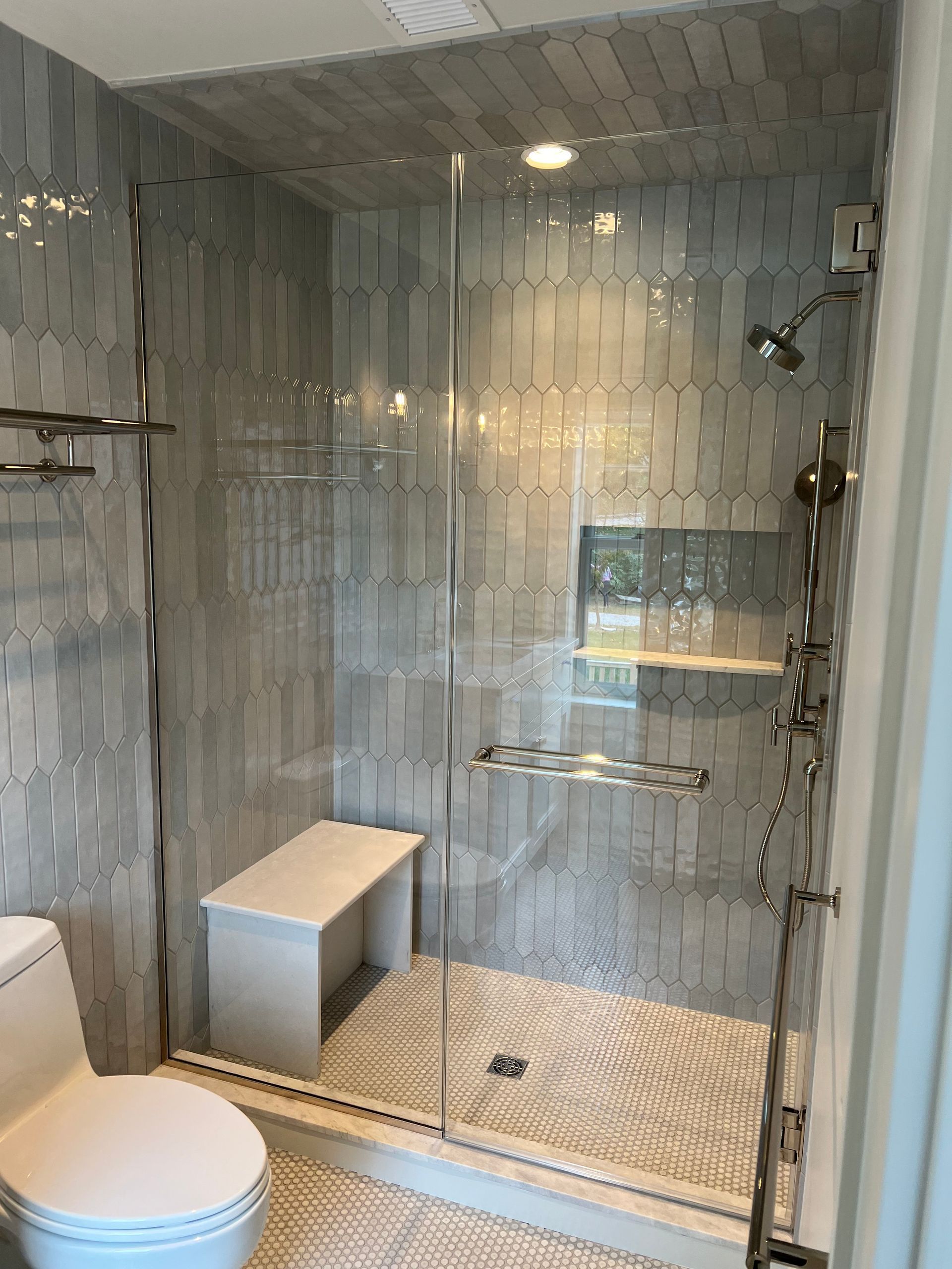 Modern bathroom with gray tiled shower, glass door, bench seat, and toilet.