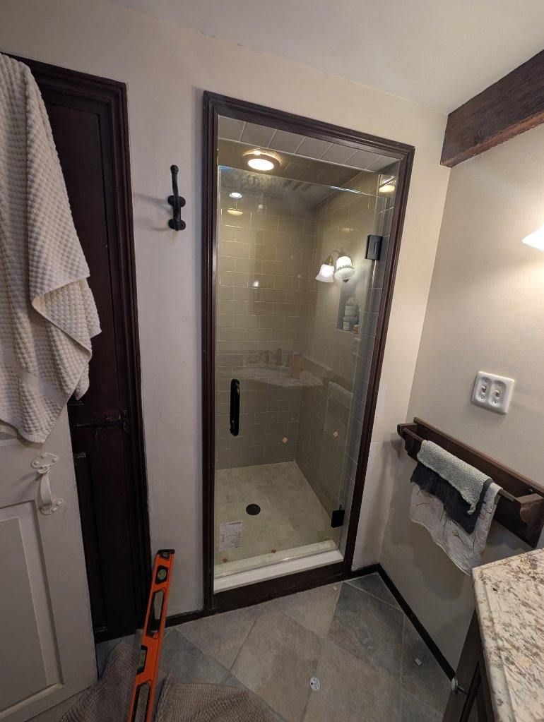 Bathroom with glass shower door, dark wood trim, towel rack, light beige walls, and granite countertop.